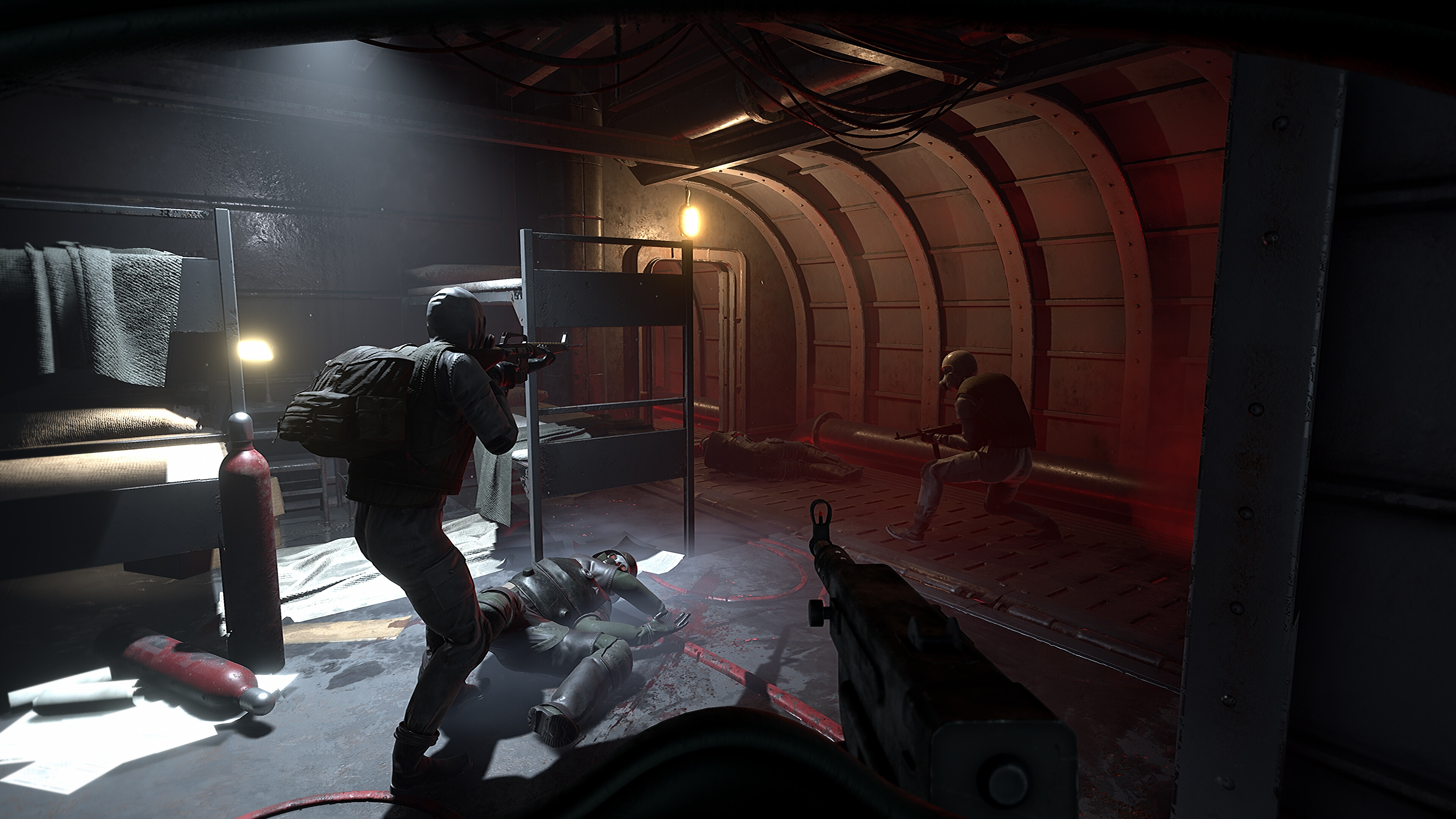 Three players stalk through a dormitory, with a dead body on the floor in front of them.