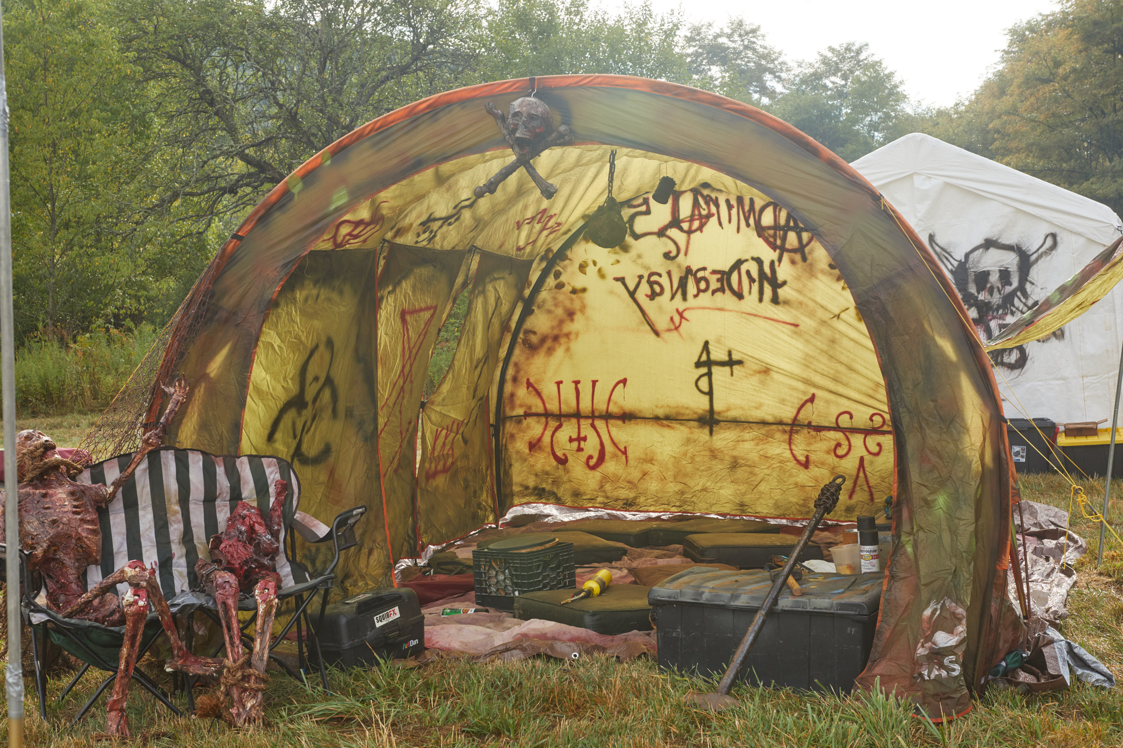 A post-apocalyptic themed tent with fake skeleton corpses sitting on a camping chair