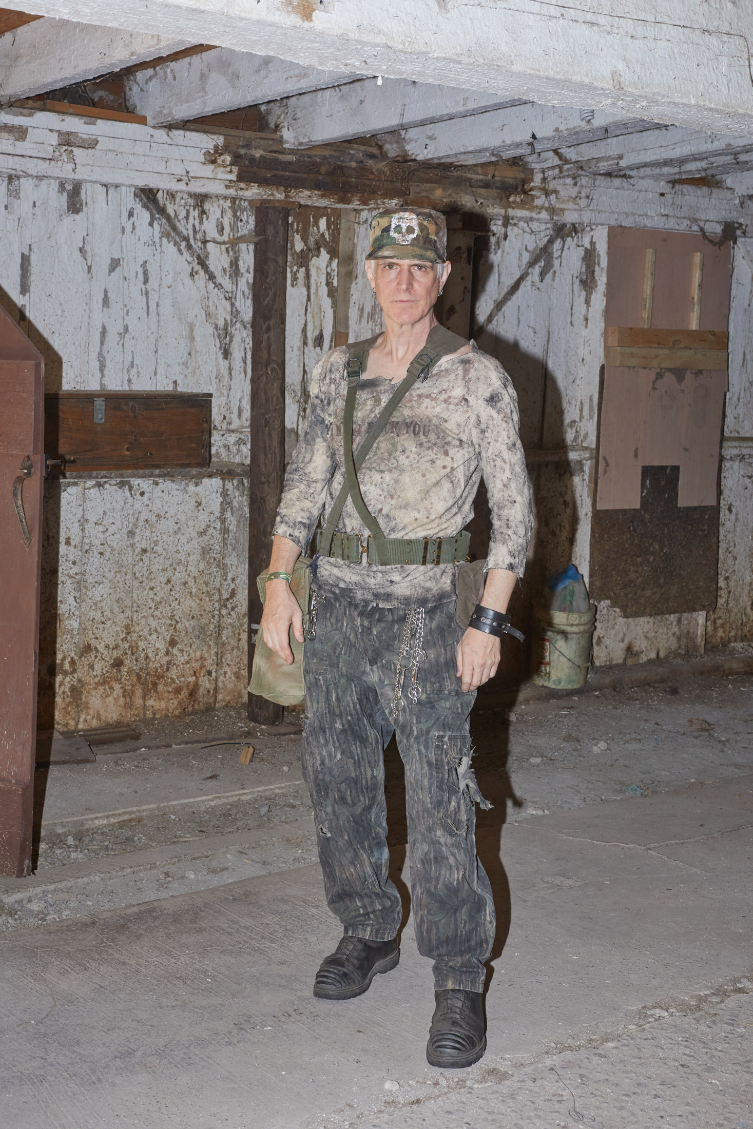 A man dressed in camouflage stands inside a dirty barn  