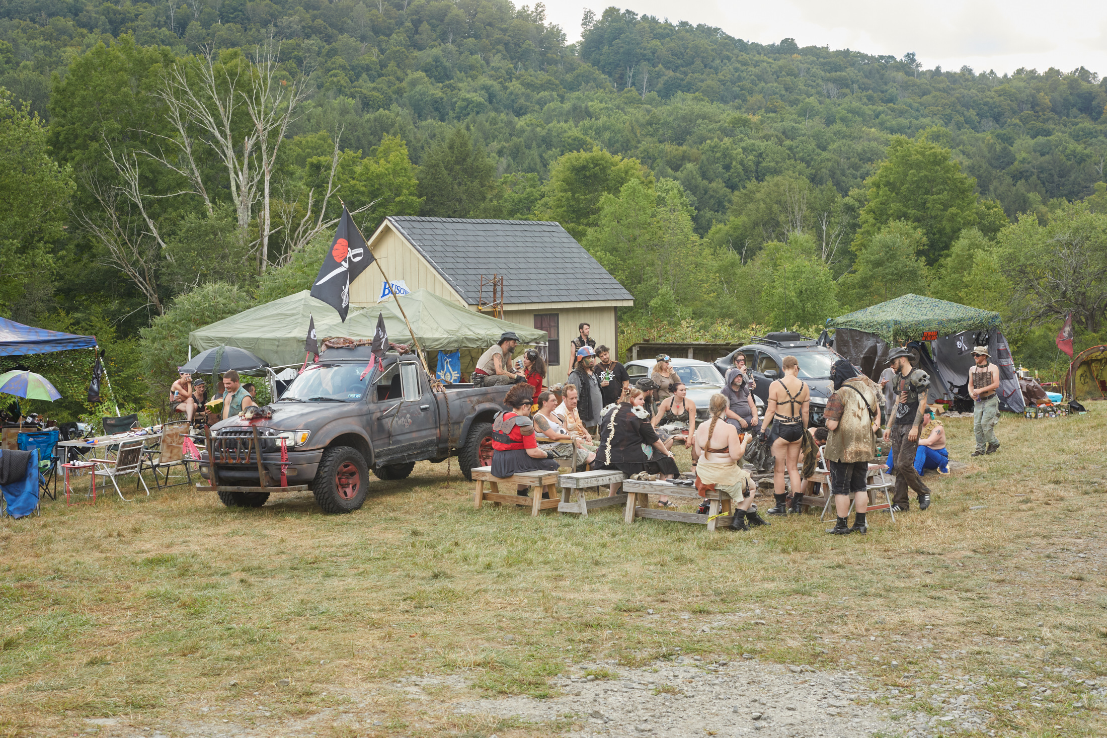 A group of attendees hang out in a field with tents and a post-apocalyptic themed truck