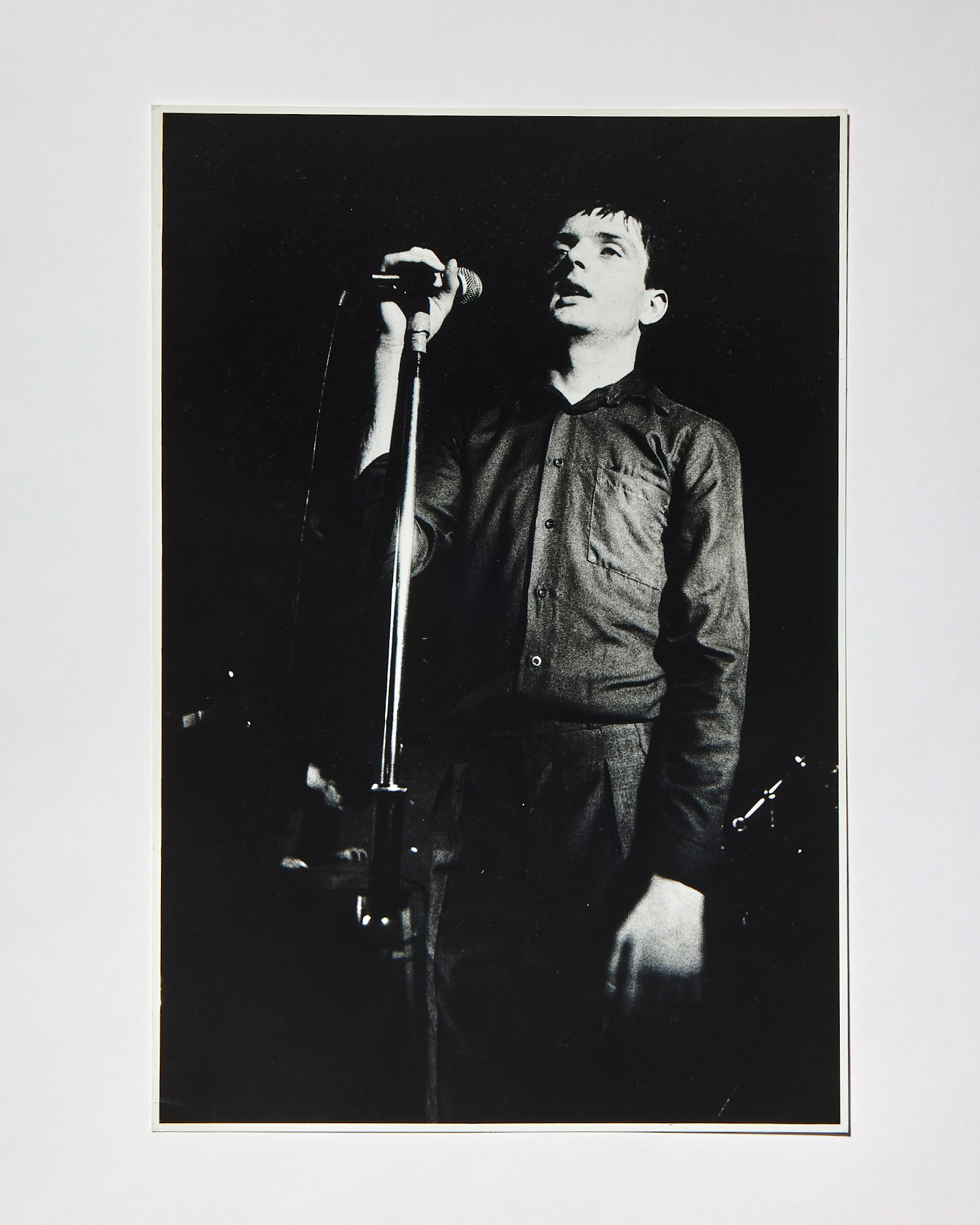 a black and white portrait of ian curtis of joy division on stage holding a microphone by kevin cummins