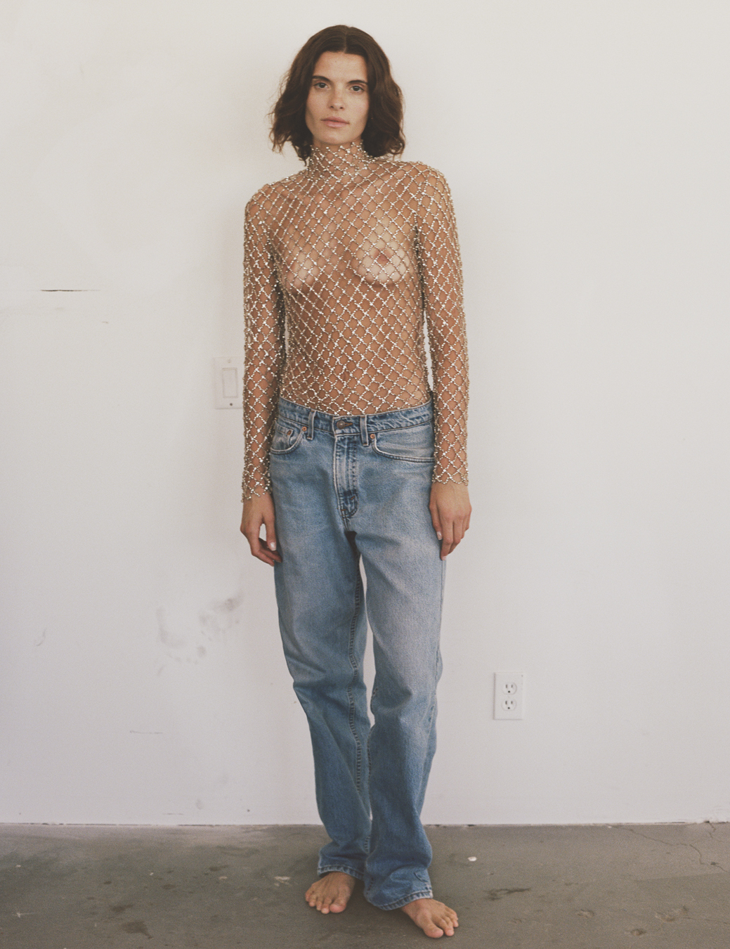 a model wears a bejewelled sheer net-type top with stonewash boyfriend jeans 