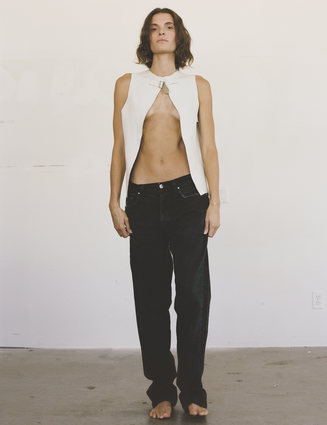 a model wears black jeans with a white open waistcoat top, her toned stomach showing