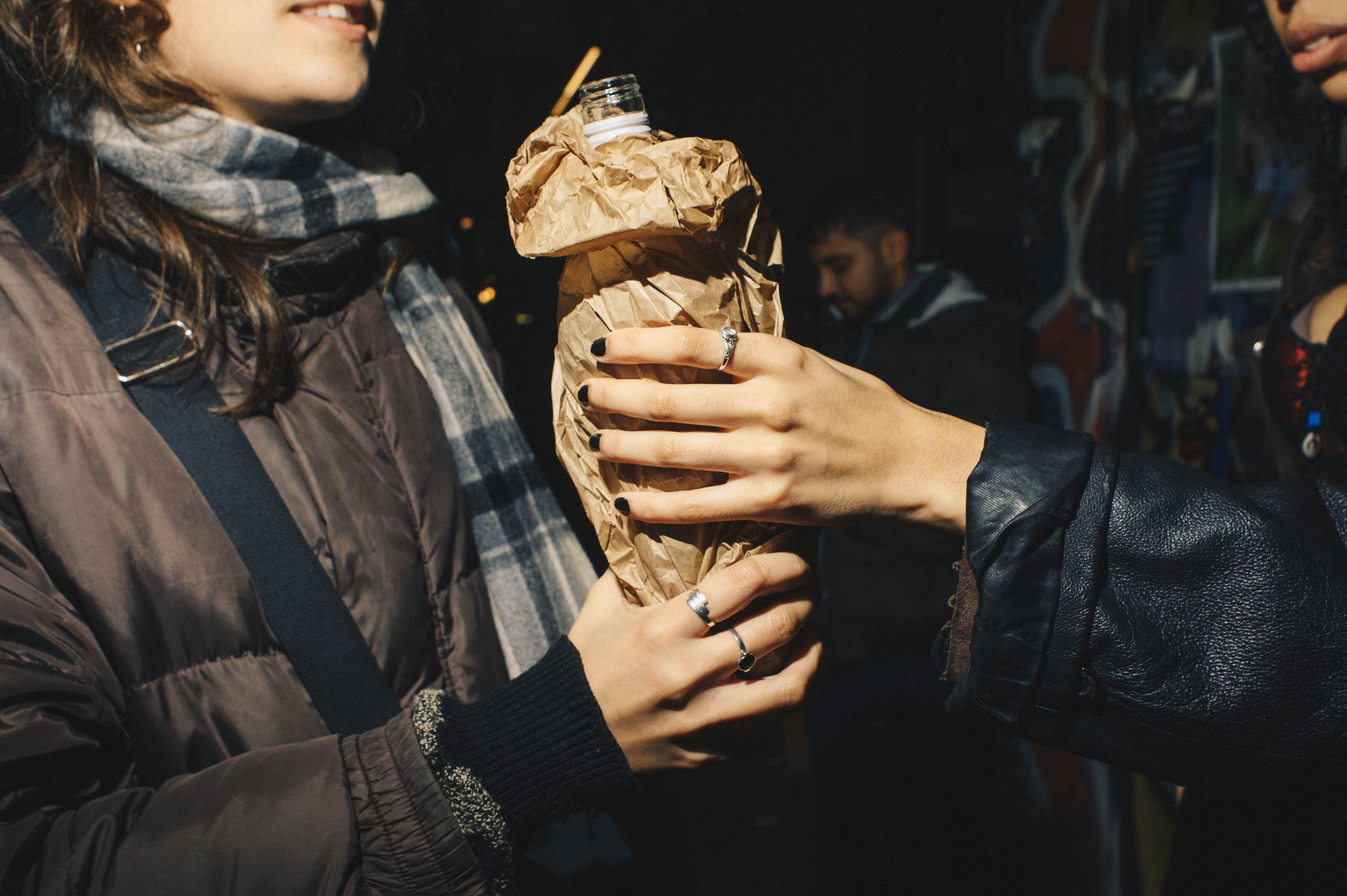 A woman passing a drink in a brown paper bag to another woman.