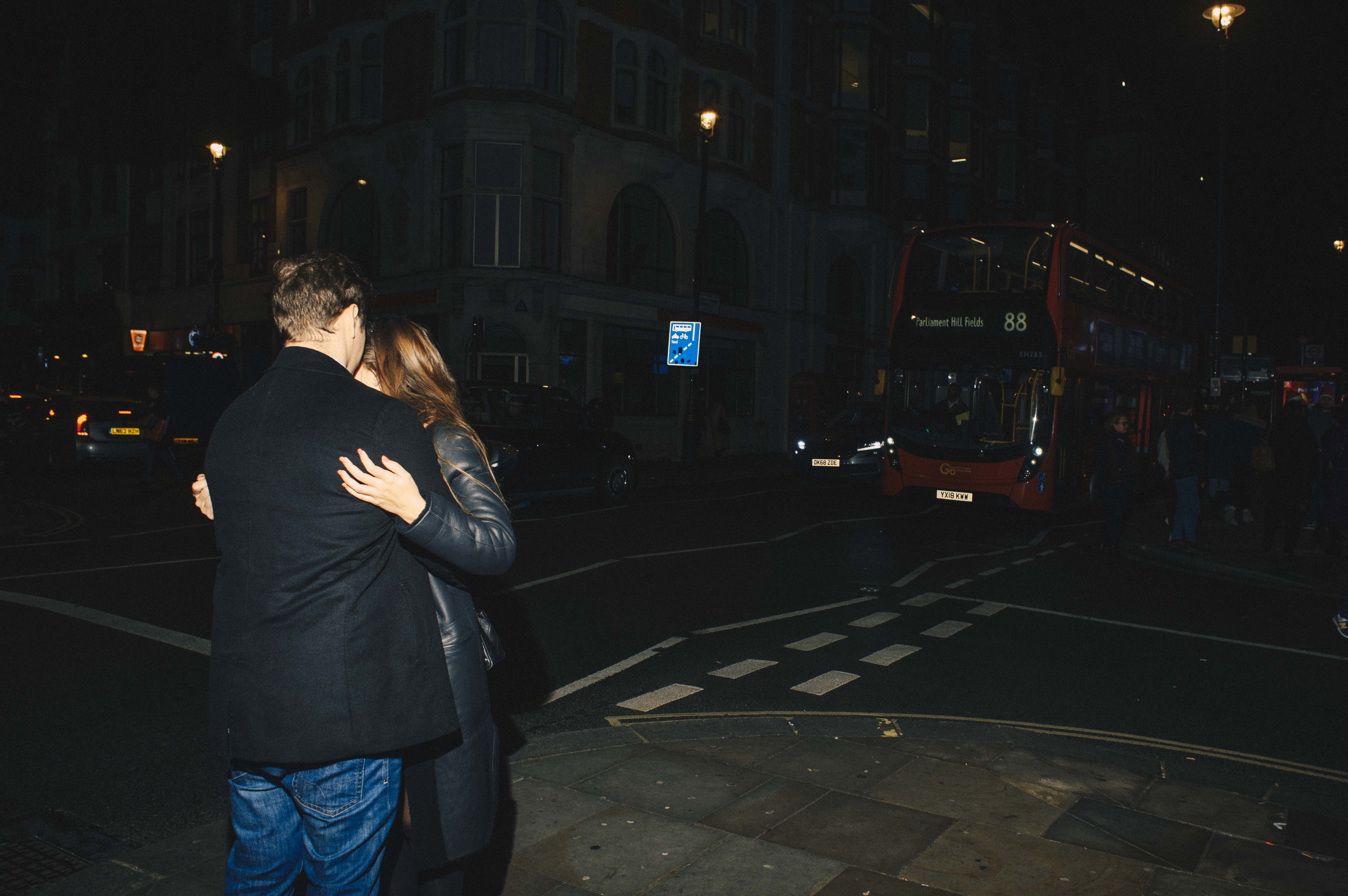 A couple embraces each other on a street corner.