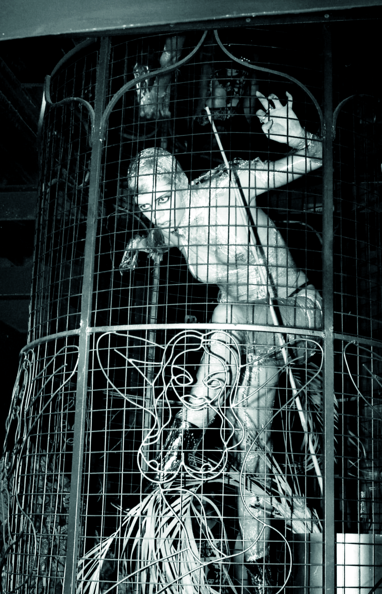 a topless person wrapped in clingfilm poses creepily inside a cage