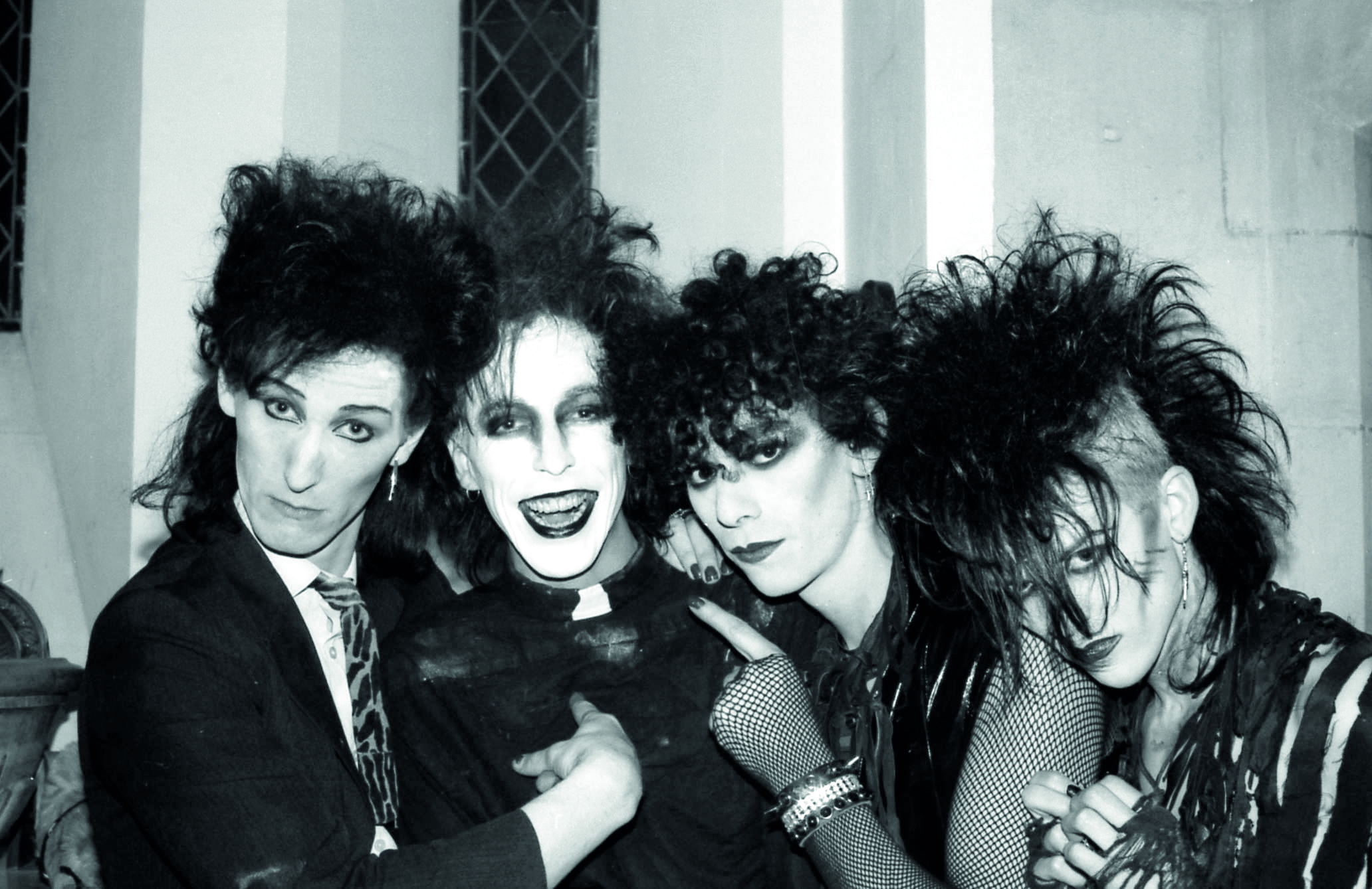 four goth friends with wild hair and dark makeup pose for a photo