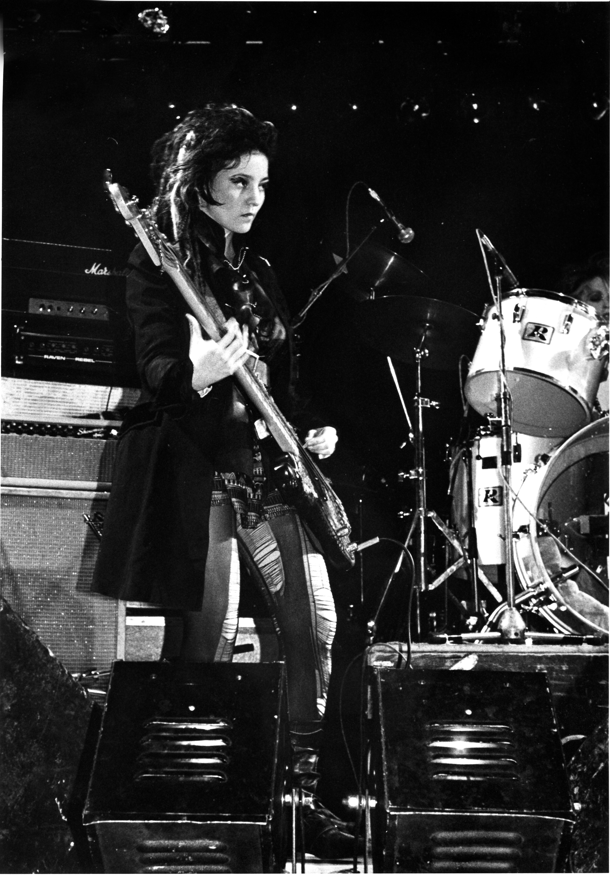 a woman with dark messy hair plays bass on a club's stage