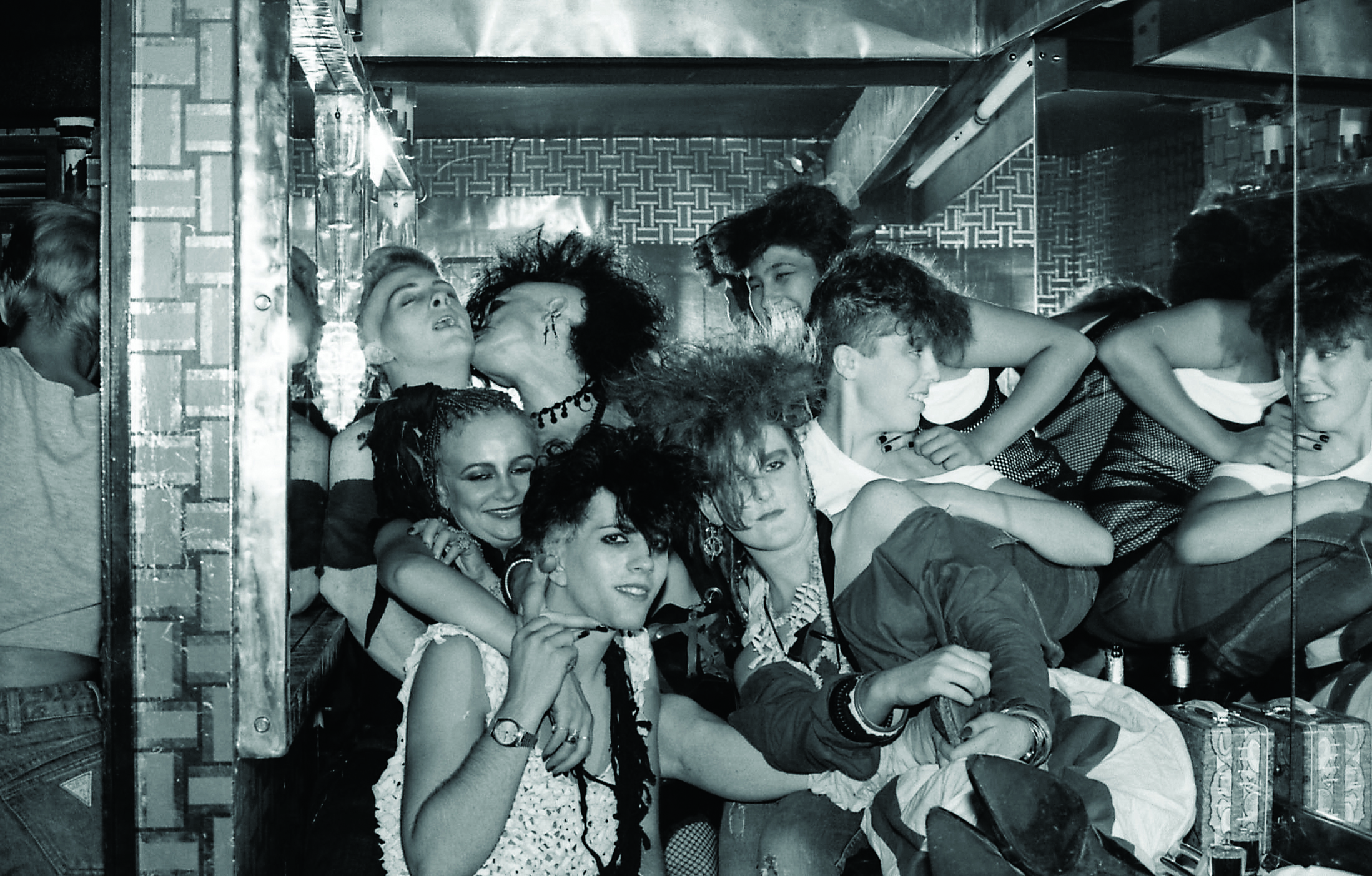 a group of 80s goths kissing and climbing on top of each other in a club toilet