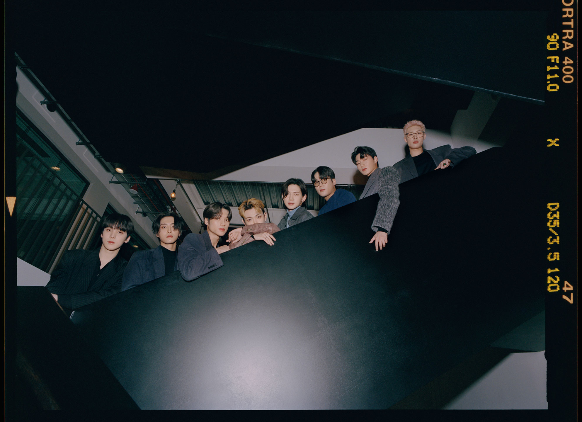 the k-pop group ATEEZ lean over the side of a floating staircase, looking to camera 