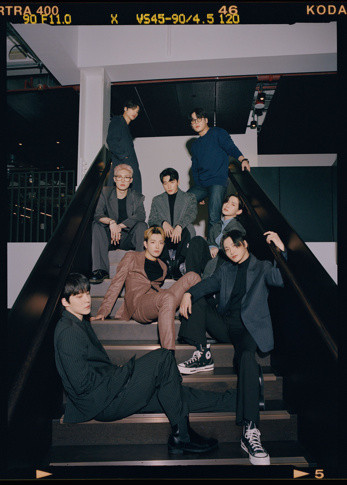 ATEEZ gather in a group, posing on a staircase wearing suits and looking to camera