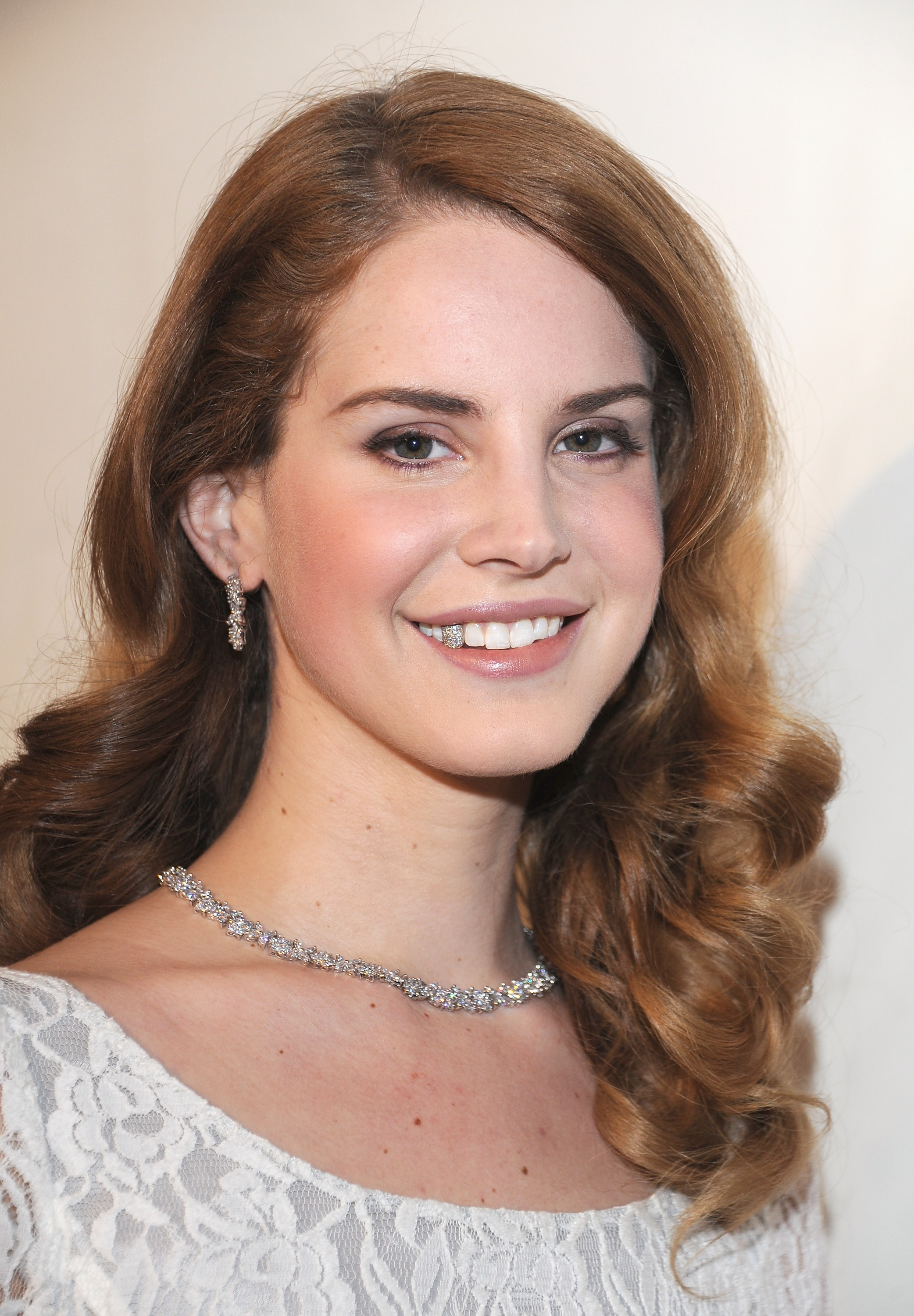 2012 Lana Del Rey smiling at an event; she wears diamond jewellery and matching grillz one one tooth