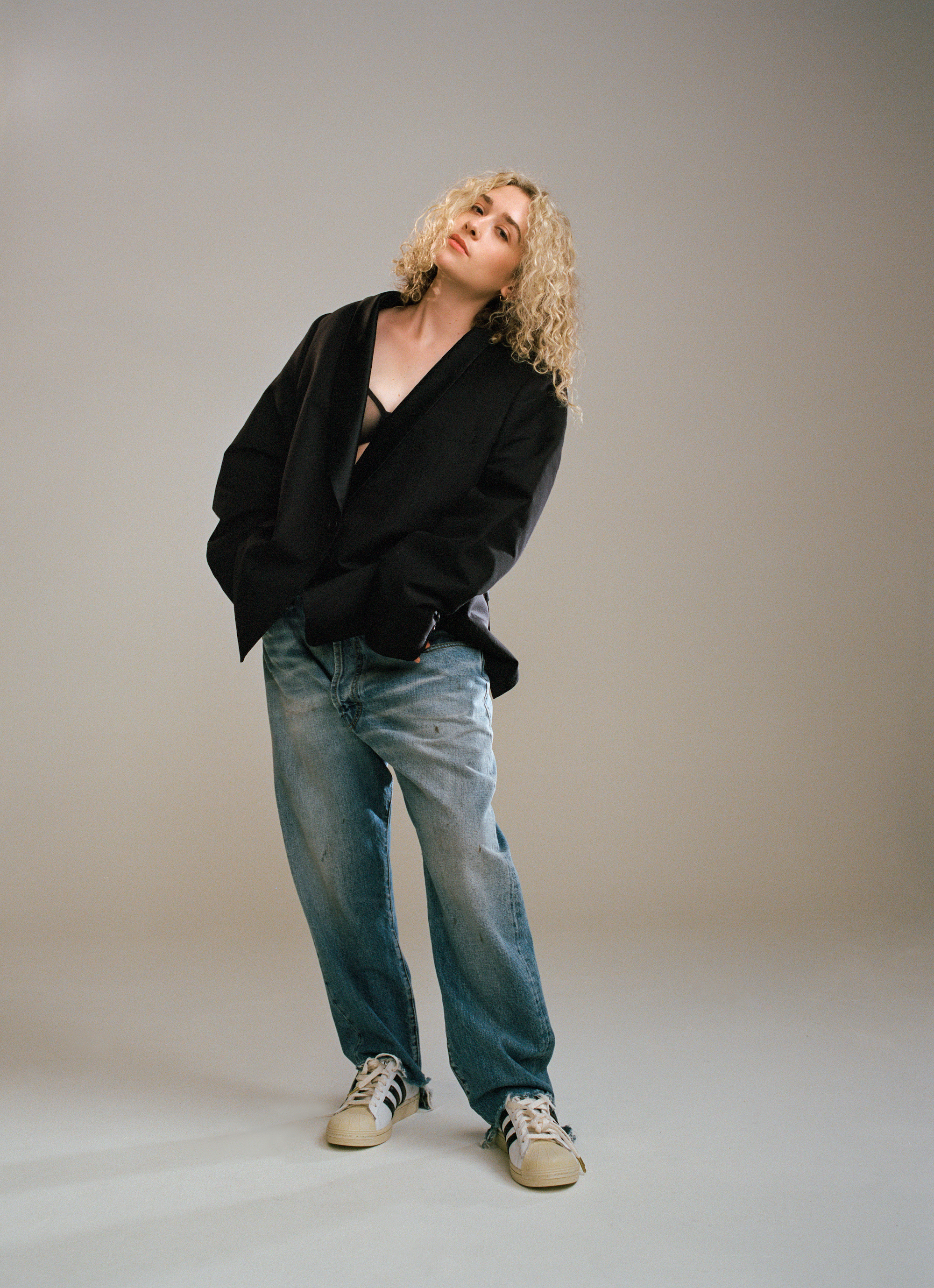 blondshell wearing blue jeans and an open blazer with her head tilted to the side