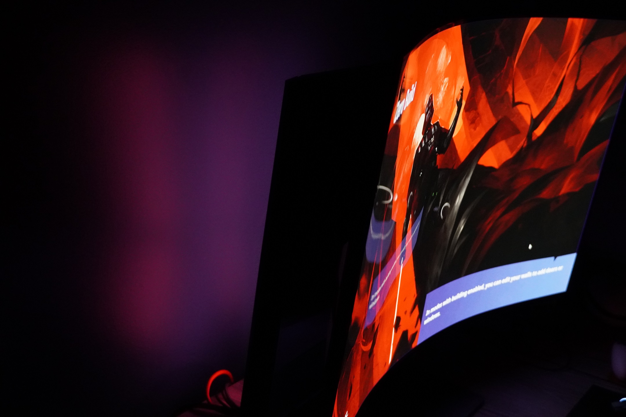 A pale wash of red light spills from the darkened shape of a monitor stand against a wall while the screen shows an image of Darth Vader against a red backdrop