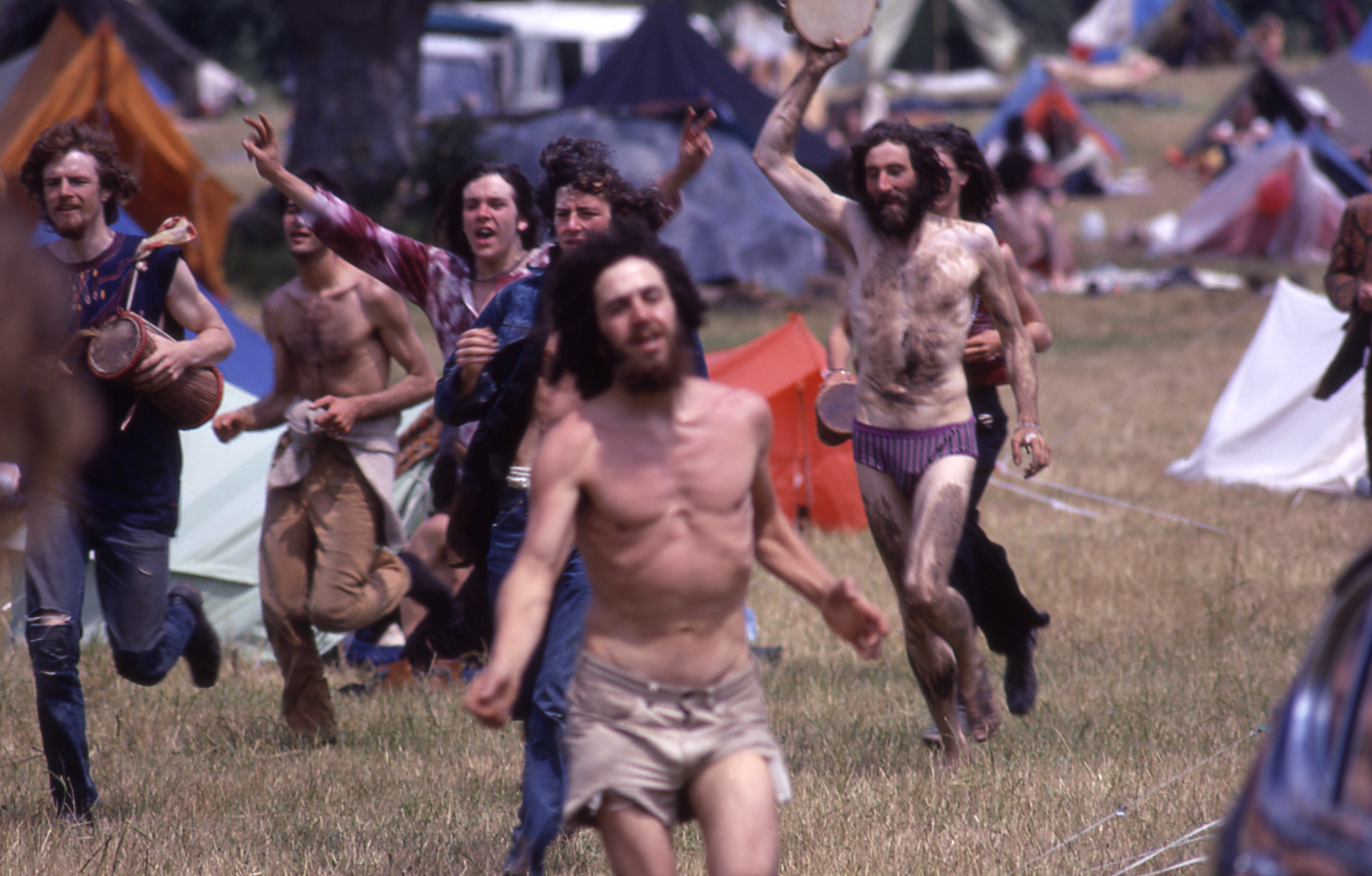 a shirtless man and Crowd Running through the field covered in mud at glastonbury 1971