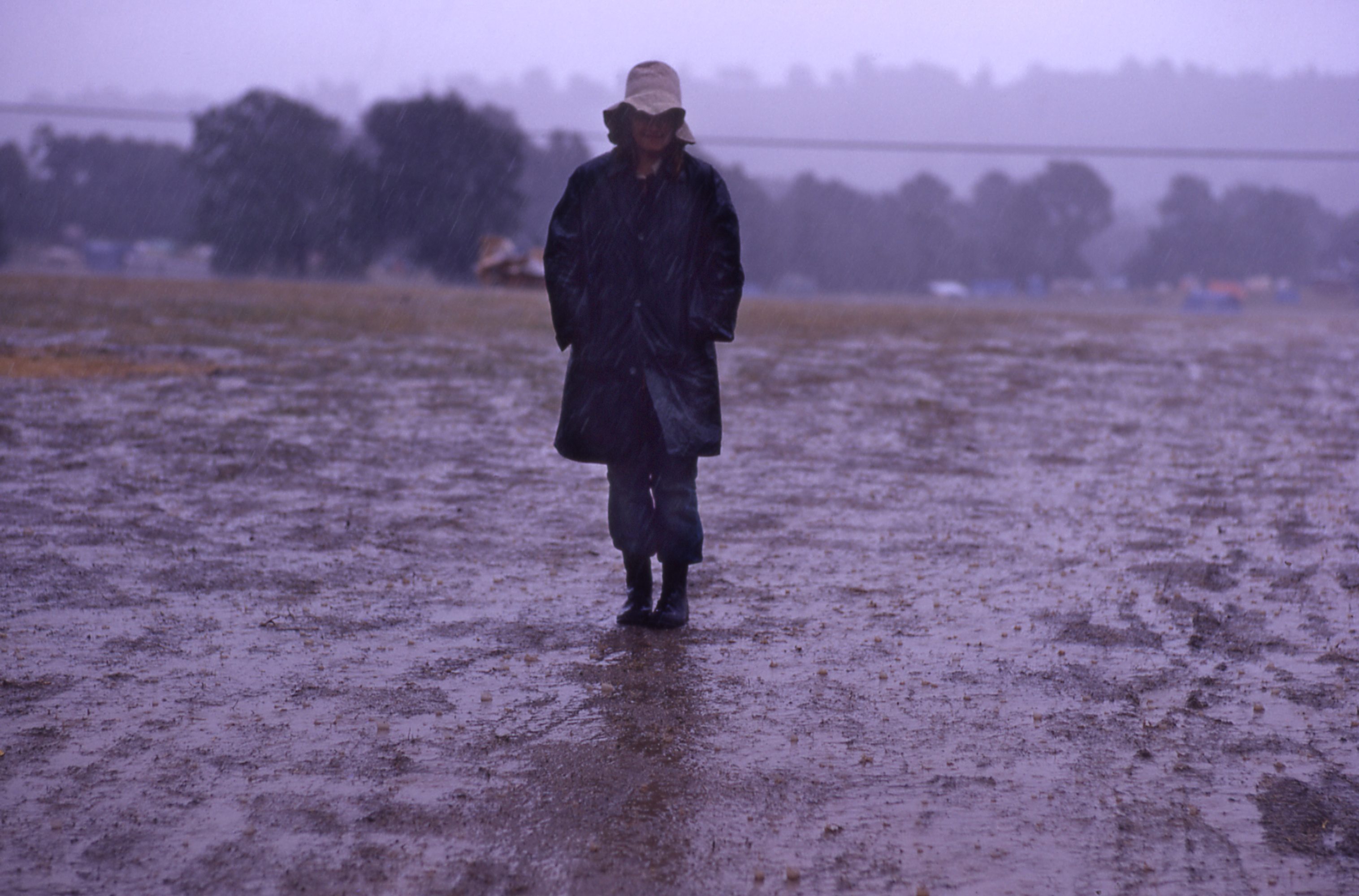 someone in a coat standing in the rain in glastonbury's muddy fields 1971
