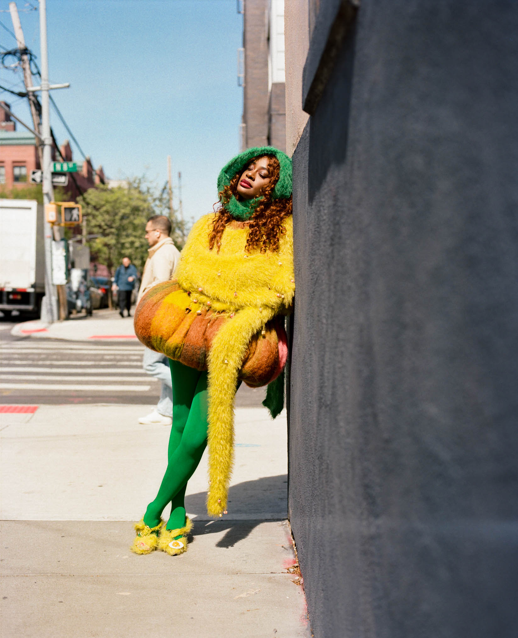 kari faux posing on a street corner in a fuzzy green and yellow costume