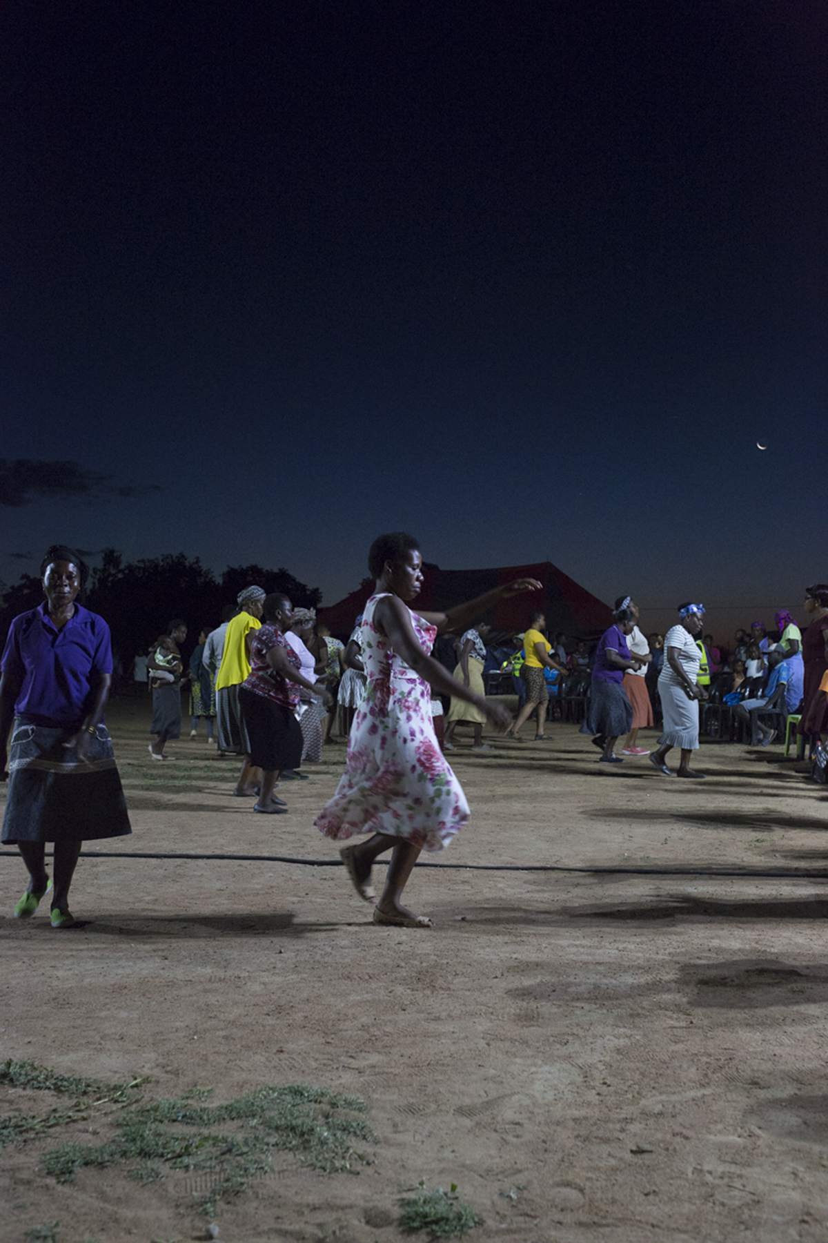 Giya Makondo-Wills, “They Came From The Water While The World Watched” – group of middle aged women dancing in front of a seated public outside at night