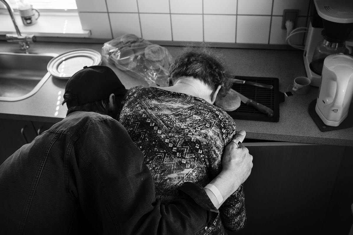 Mikkel Hørlyck, Jørgen, a Mystery – pedersen hugging his mother from behind, as she is bent over a kitchen countertop, cutting a small bread