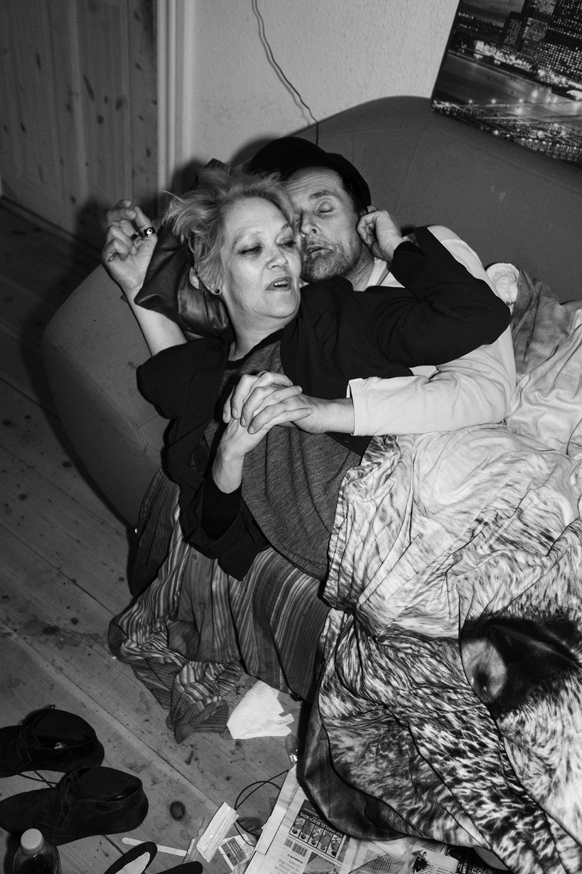 Mikkel Hørlyck, Jørgen, a Mystery – Man and woman lying on a couch. Pedersen is hugging her from behind, the floor is quite messy.