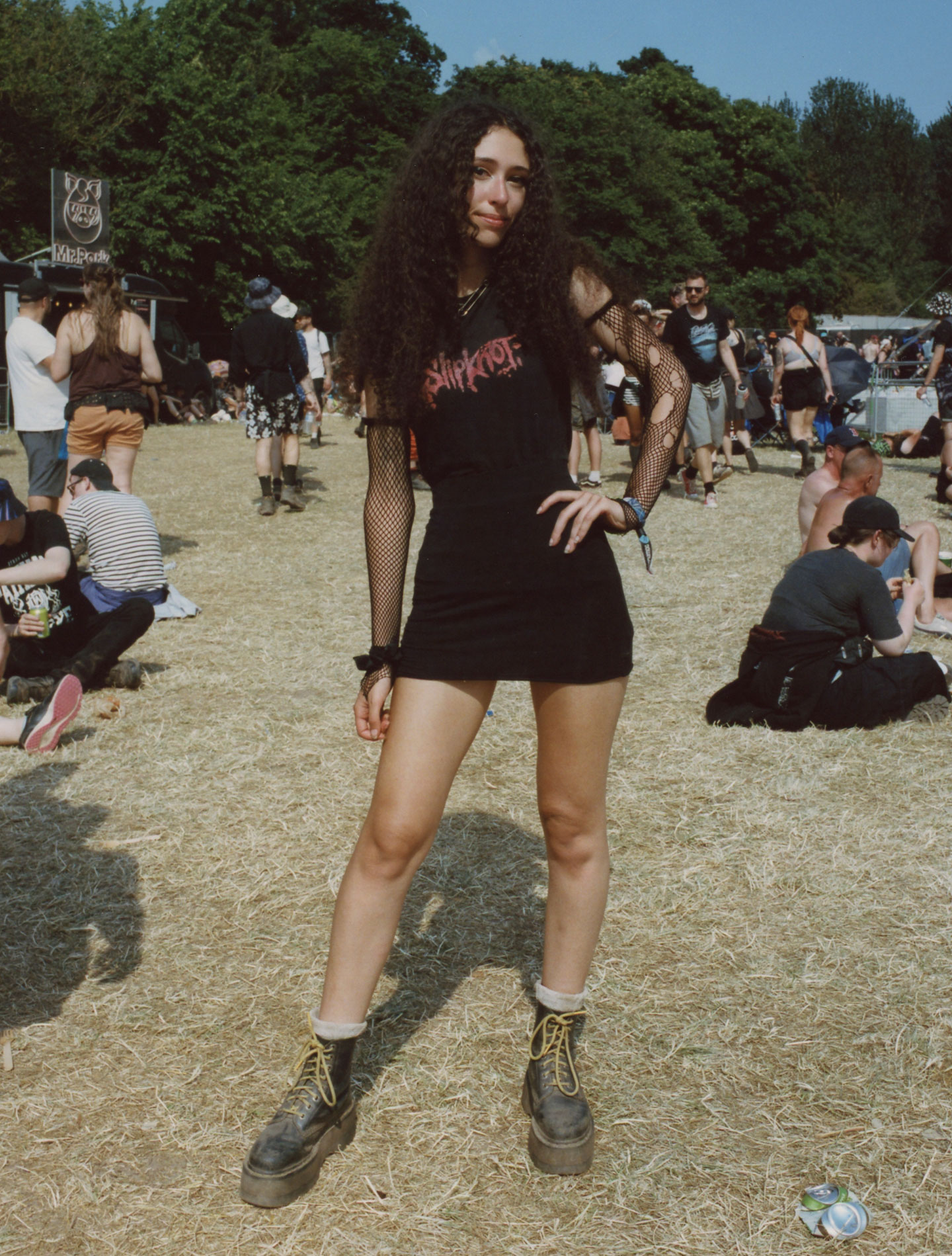 a teen girl with long curly hair wears docs and a slipknot tee with fishnet tights on her arms