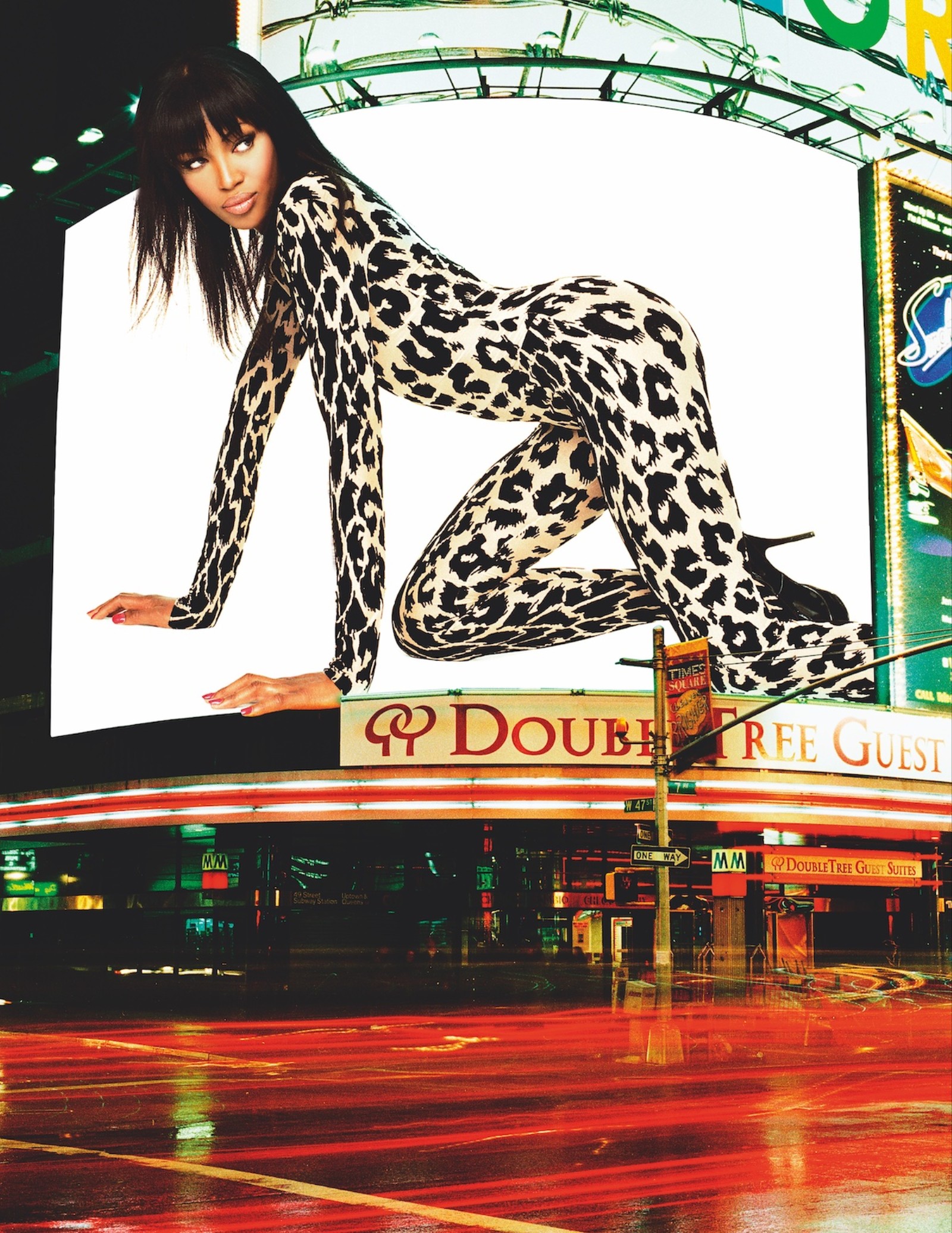 naomi campbell in a leopard print catsuit on a billboard in a brightly lit cityscape