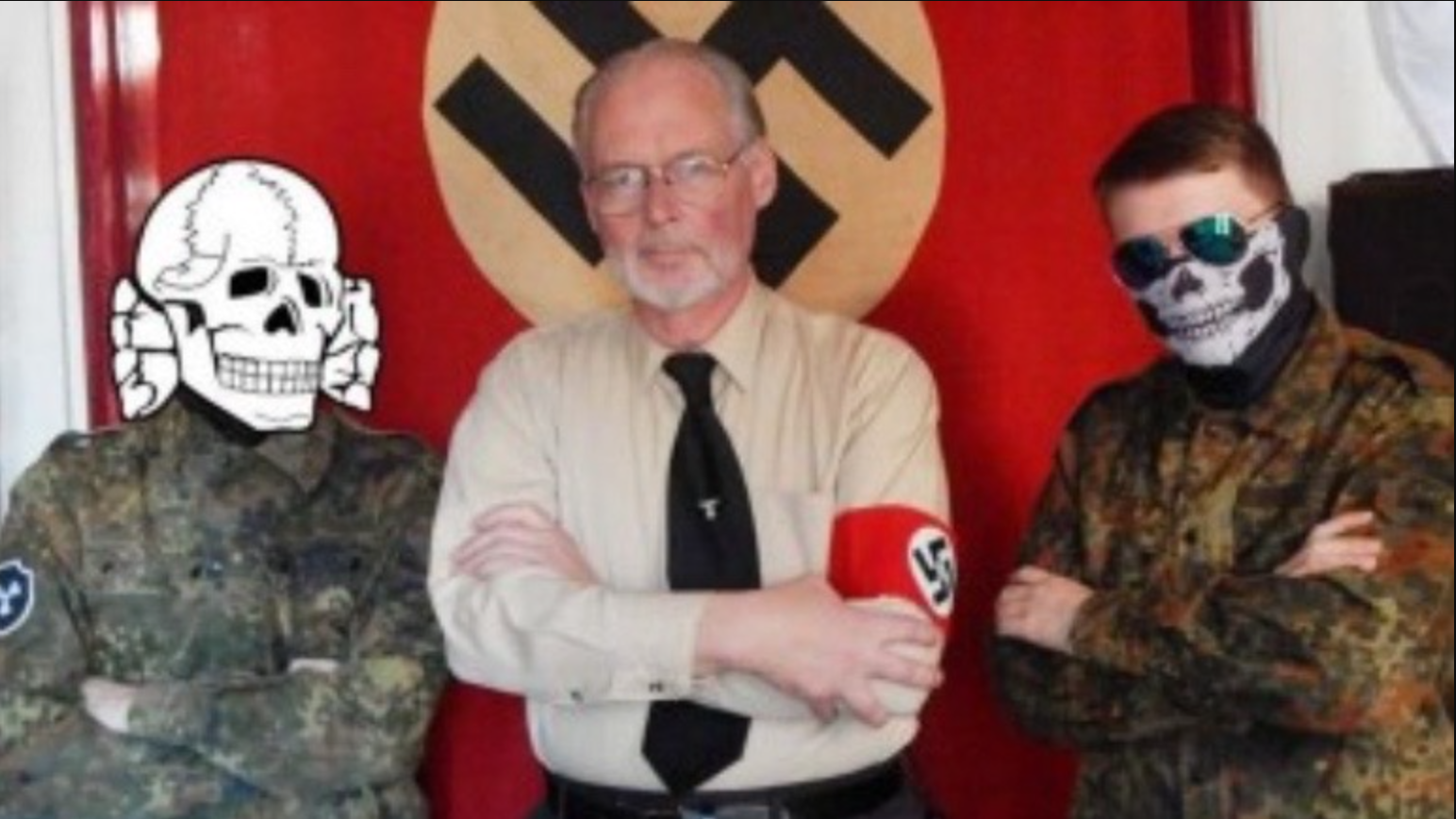 Ein älterer Mann in Nazi-Uniform posiert vor einer Hakenkreuzflagge neben zwei jungen Männern in Tarnkleidung und verdeckten Gesichtern