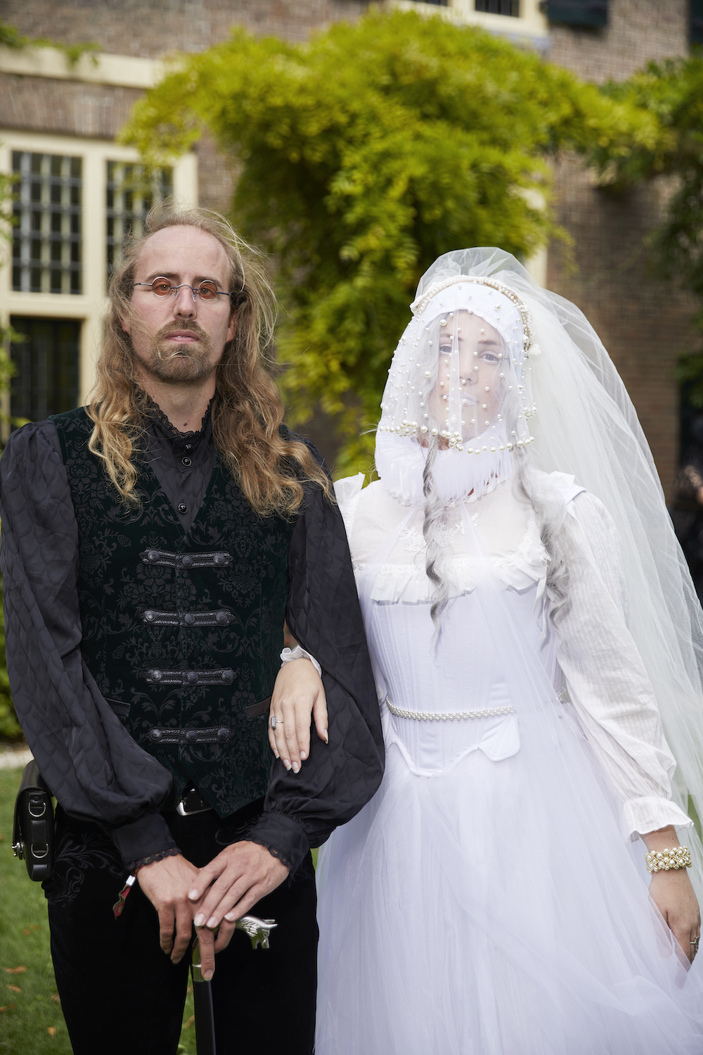 Ein Mann in einem schwarzen viktorianischen Outfit mit Gehstock und eine Frau in einem weißen Tüllkleid mit Gesichtsschleier