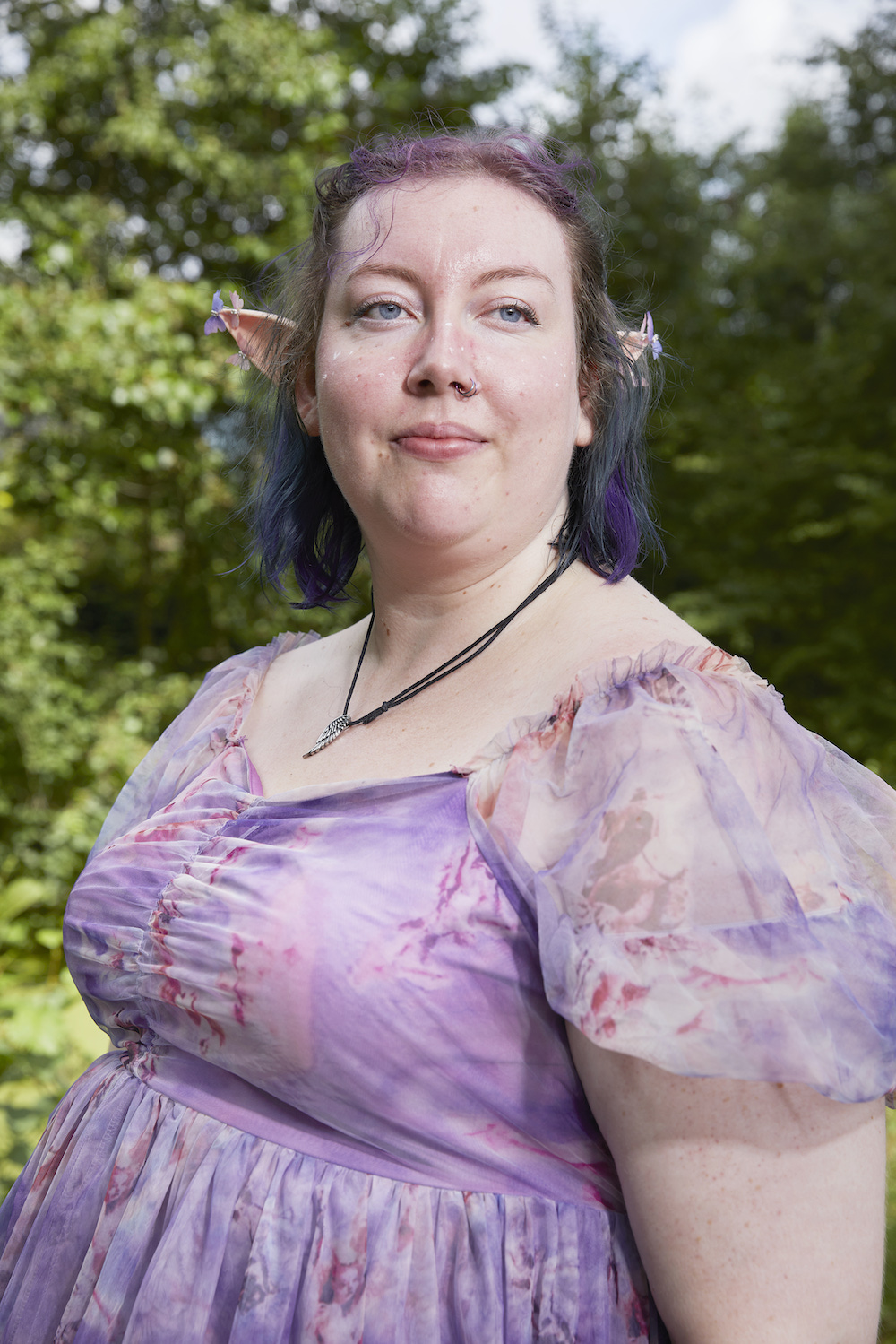 Eine Frau mit Elfenohren und lila-grün gefärbten Haaren und einem lila Kleid
