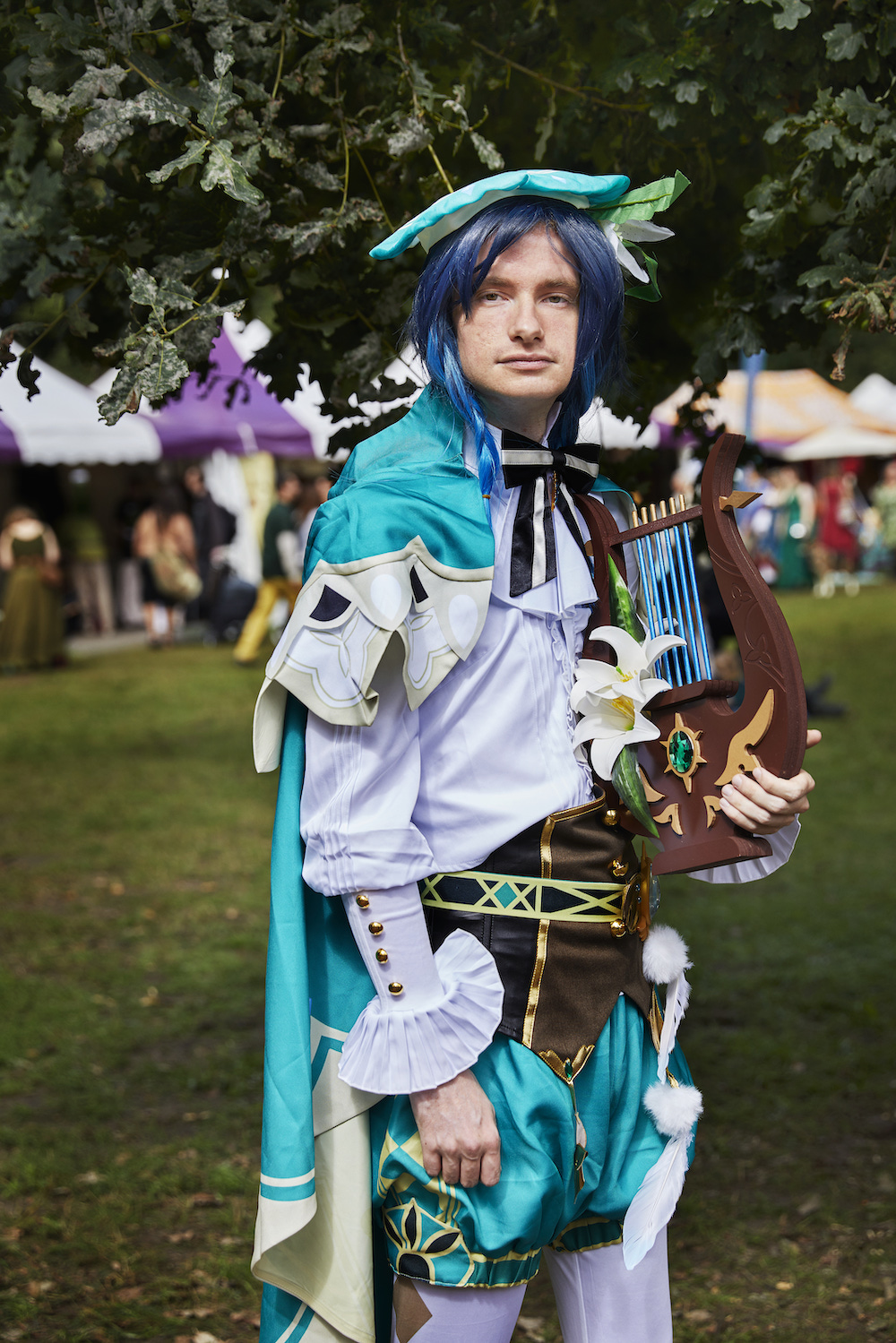 Ein Mann mit blauen Haaren und einem farbenfrohen Bardenoutfit mitsamt Harfe
