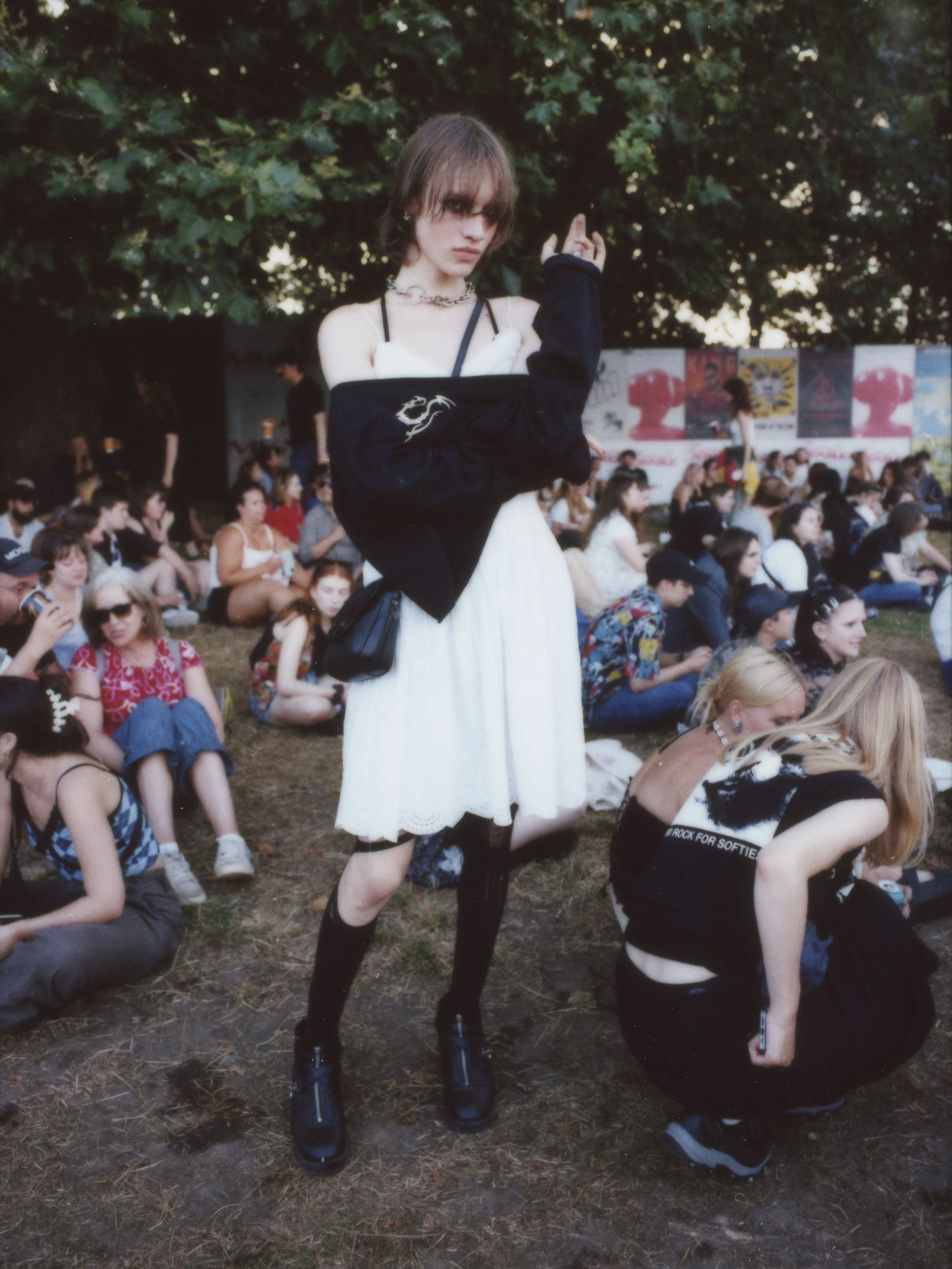 a femme presenting person in a white slip dress and knee high socks posing subtley with a jumper over their arms; they have dark smoky eye makeup photographed by Jody Evans