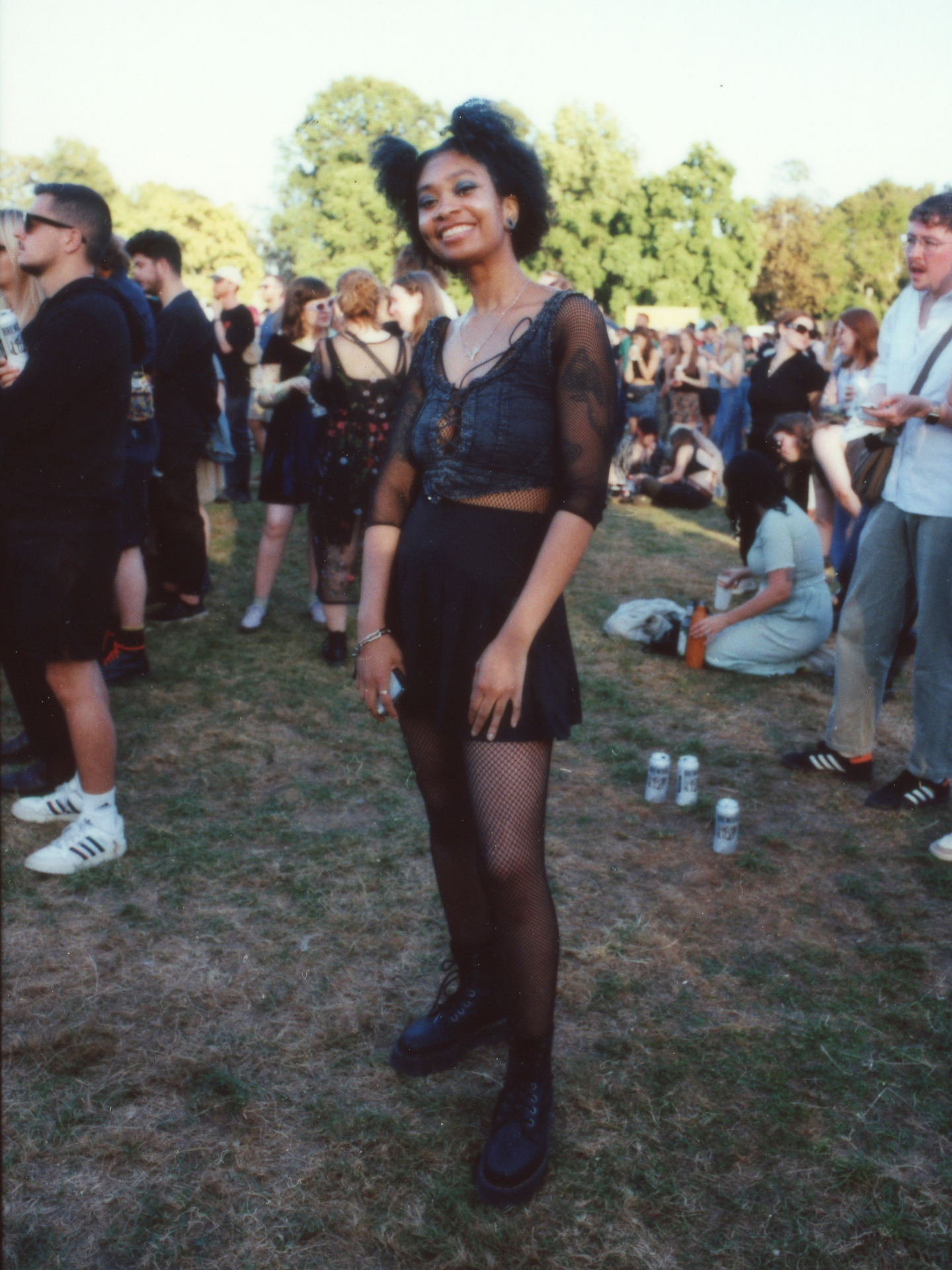 a woman with an afro tied in cute bunches wears a gothic corset top, a tennis skirt and fishnet tights with docs; she smiles to the camera photographed by Jody Evans
