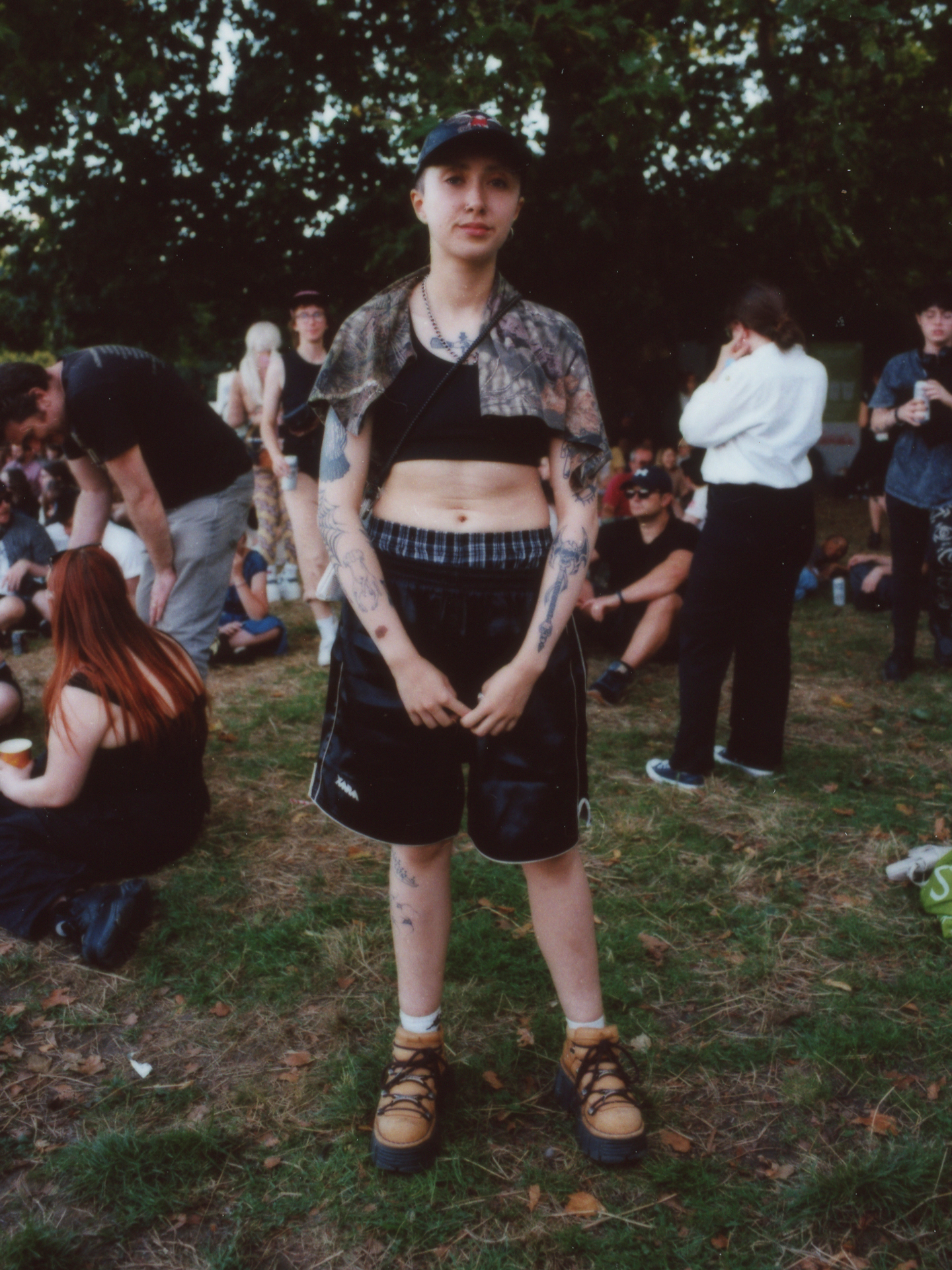 a tattooed festival-goer wearing boxing shorts with a sports bra stands for a portrait photographed by Jody Evans