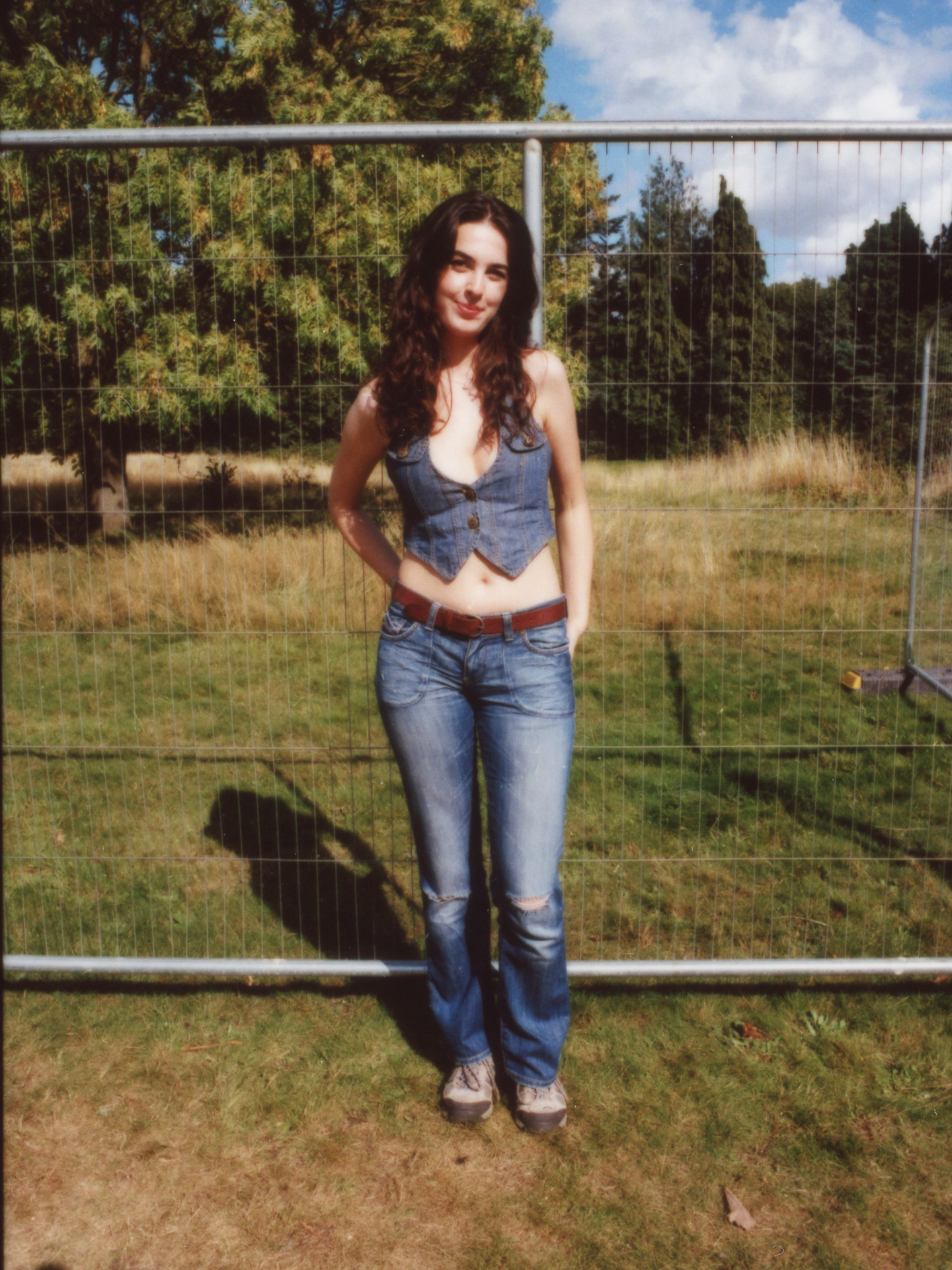 a festival-goer with long curly hair wears a double denim look – matching jeans and waistcoat with nothing underneath photographed by Jody Evans