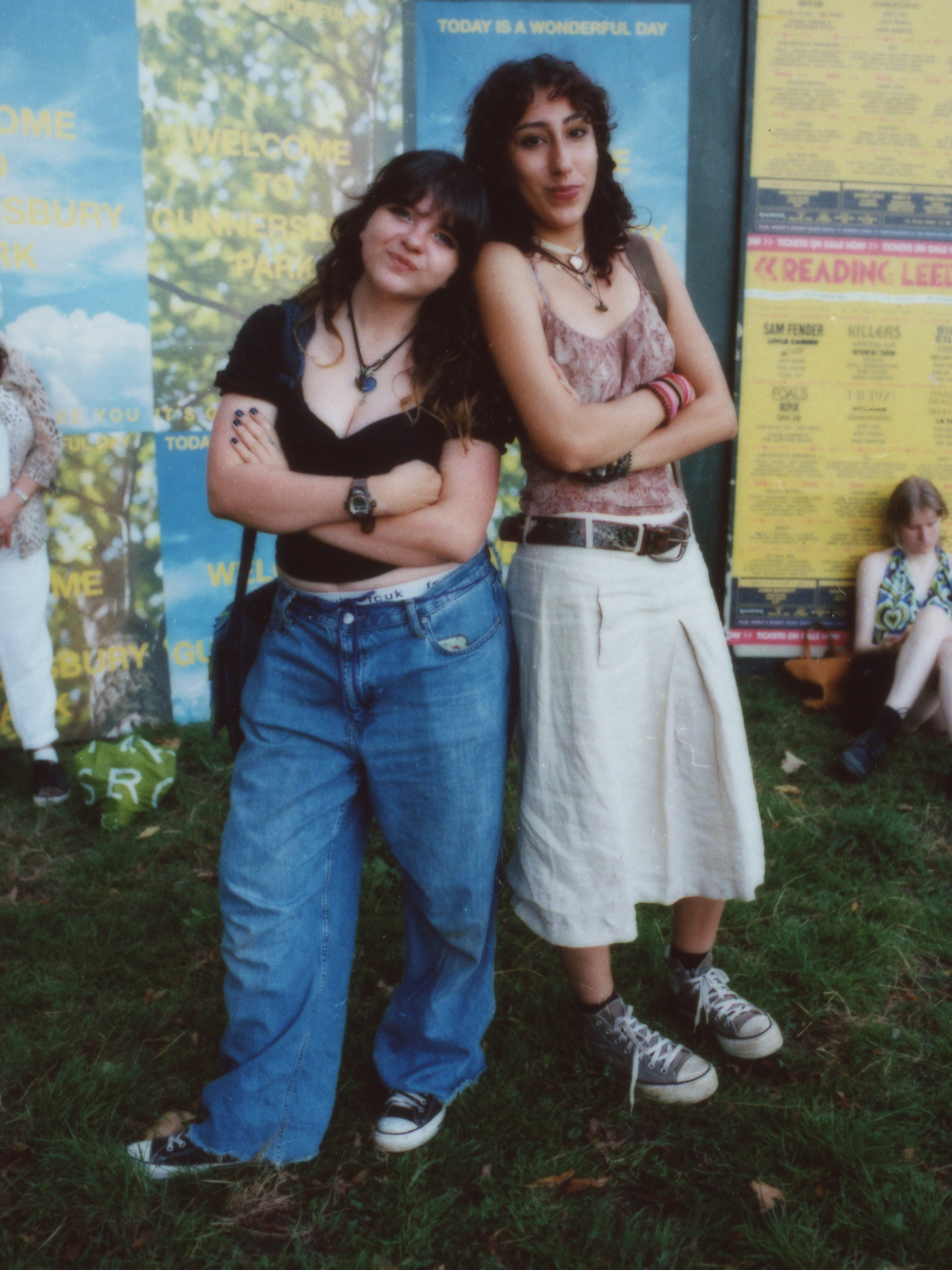 two young festival-goers wearing converse stand almost back to back with their arms crossed photographed by Jody Evans