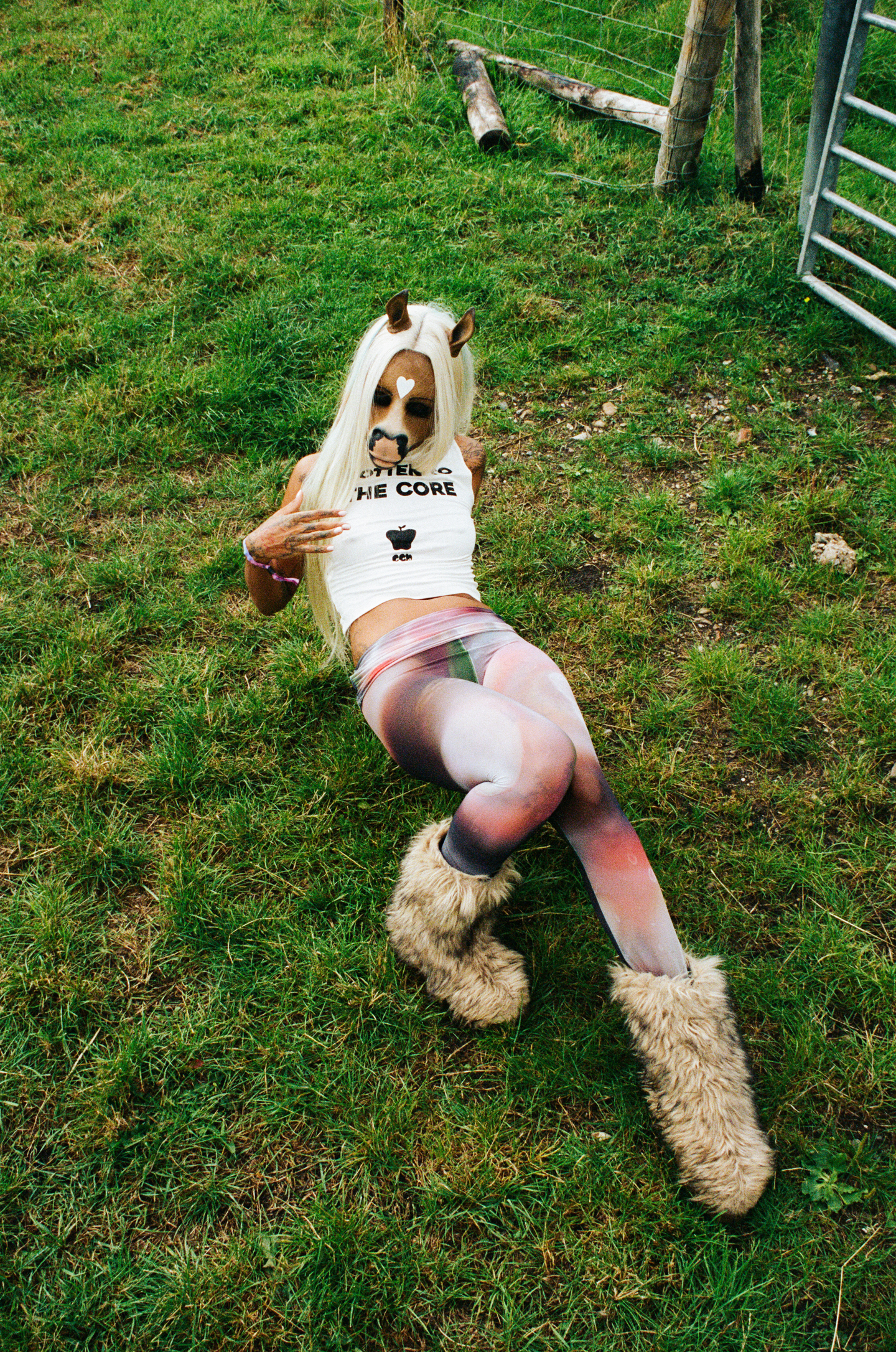 the DJ horsegiirL reclines in the grass in a tank top, leggings and furry boots 