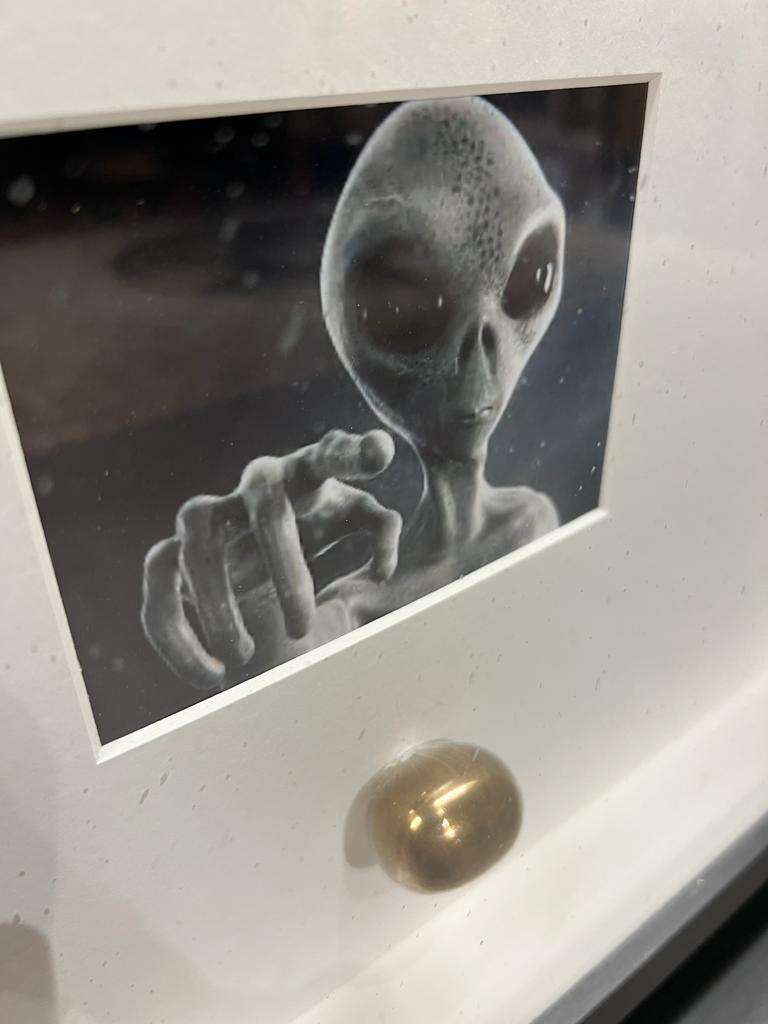 Ein Bild von einem Alien und darunter eine goldene Kugel. 