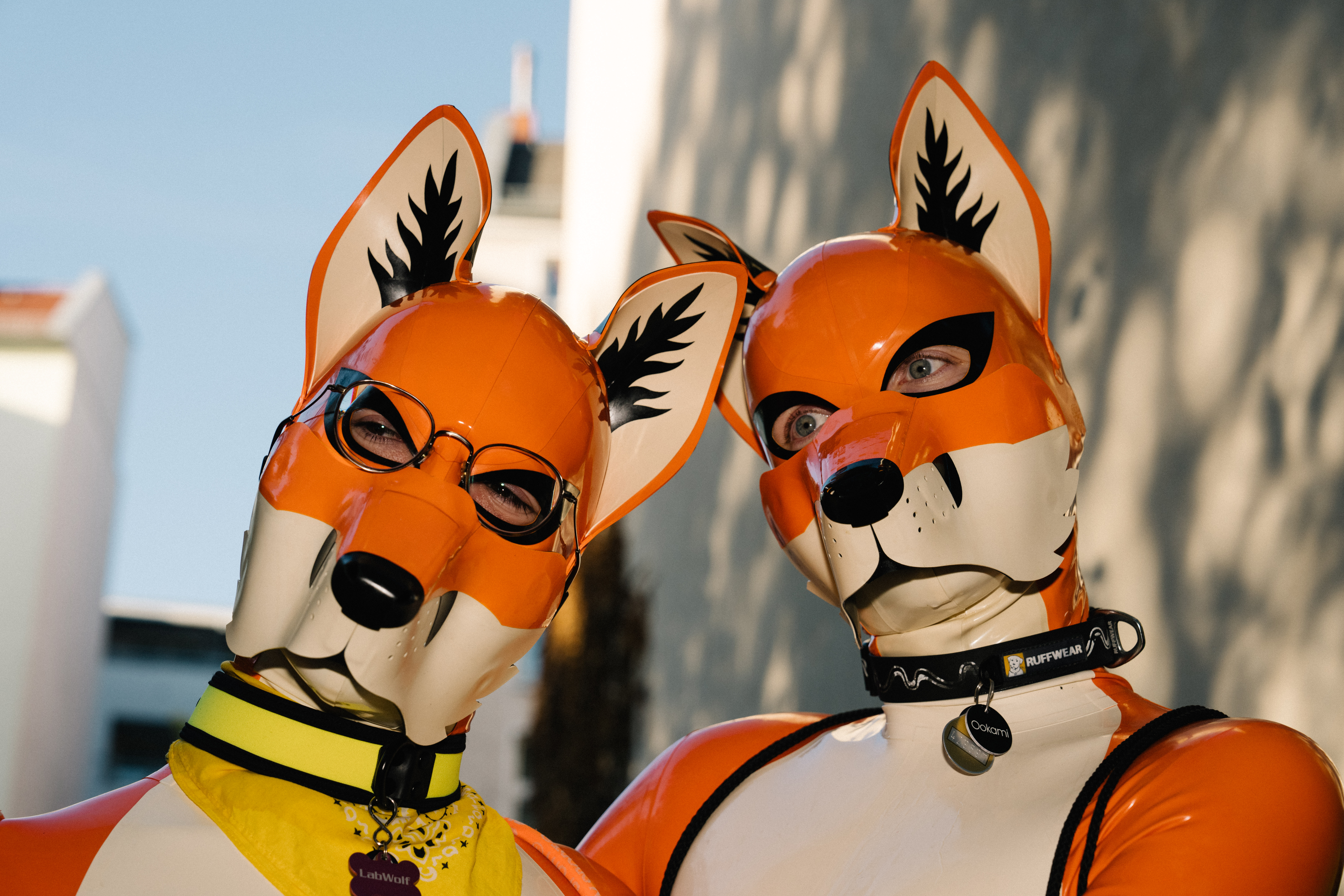 Zwei Personen tragen orangefarbene puppy play outfits aus Latex bei einem Fetischevent