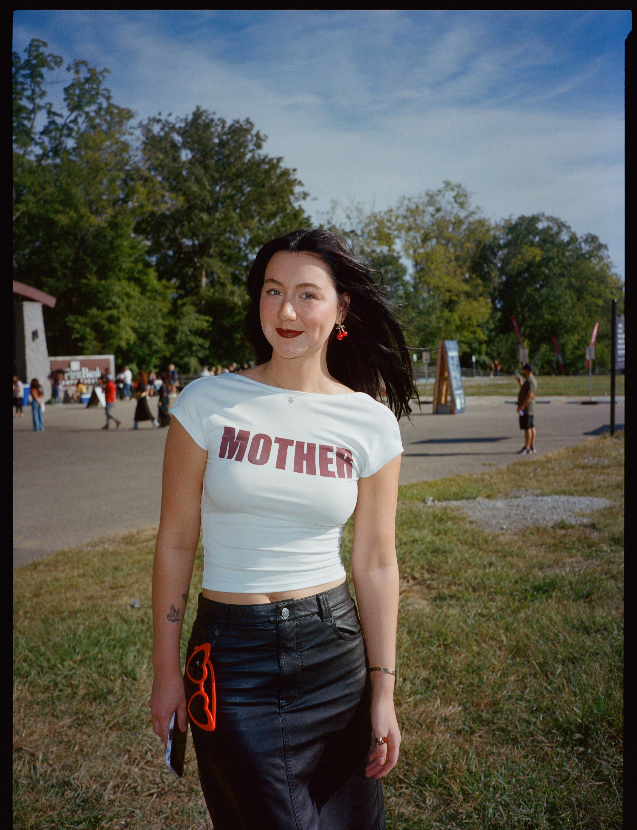 a lana del rey fan stands outside one of her shows, she is wearing a t-shirt that says 'mother' in red writing and a black leather skirt.
