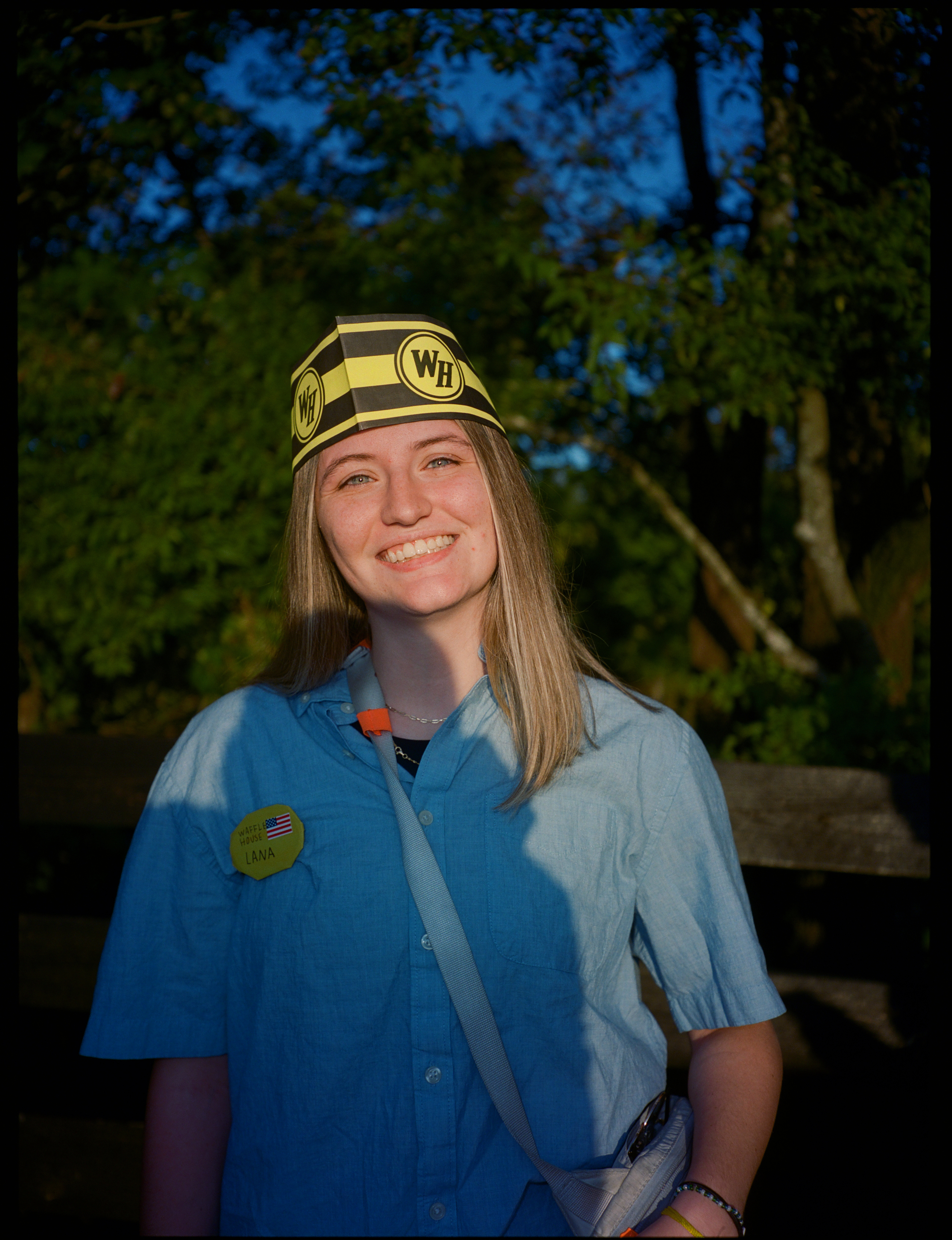 a lana del rey fan dressed up like she works in waffle house, with a blue shirt and a cap with the waffle house logo on it