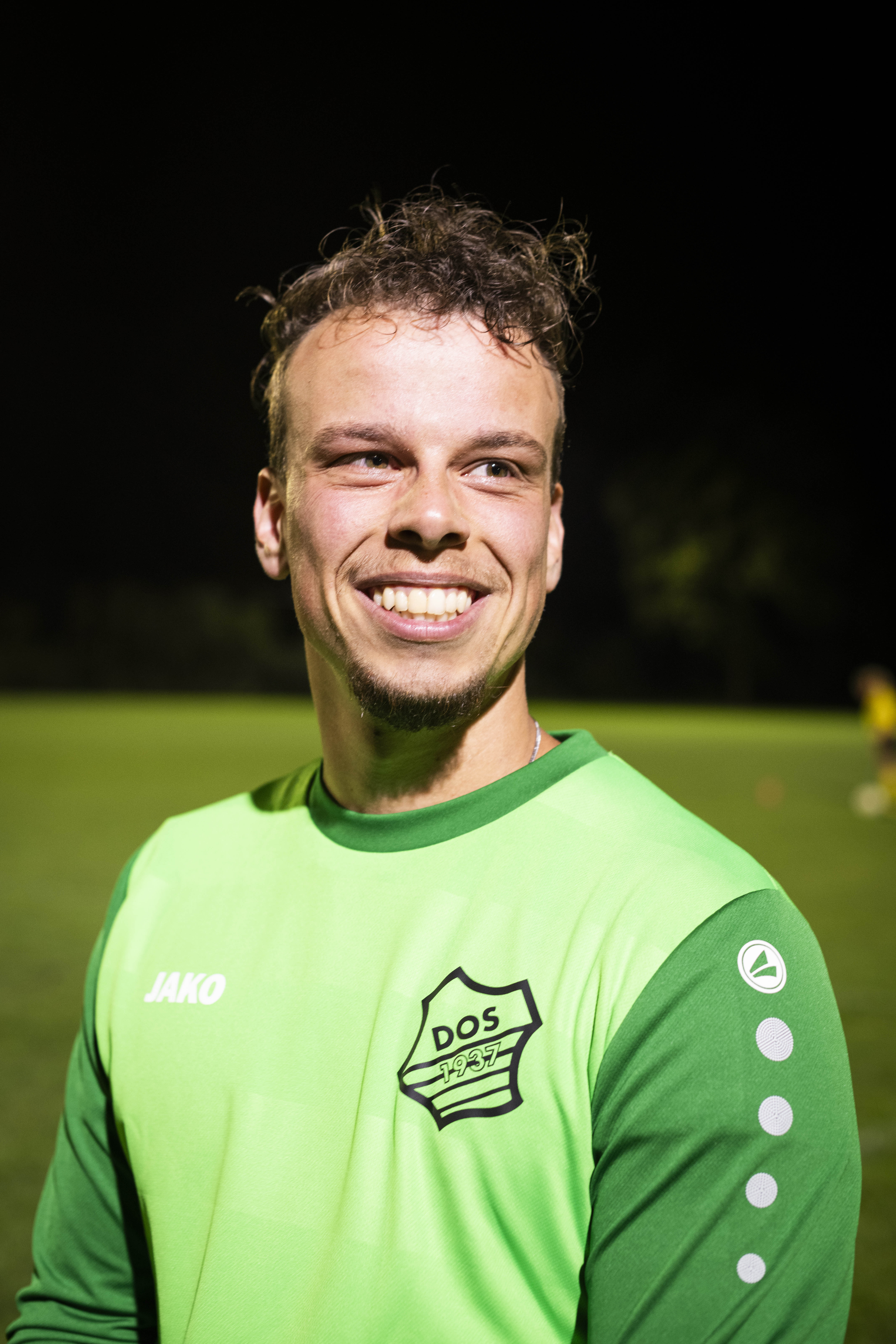 portrait of a football player smiling, they're dressed in a long-sleeved green sports top