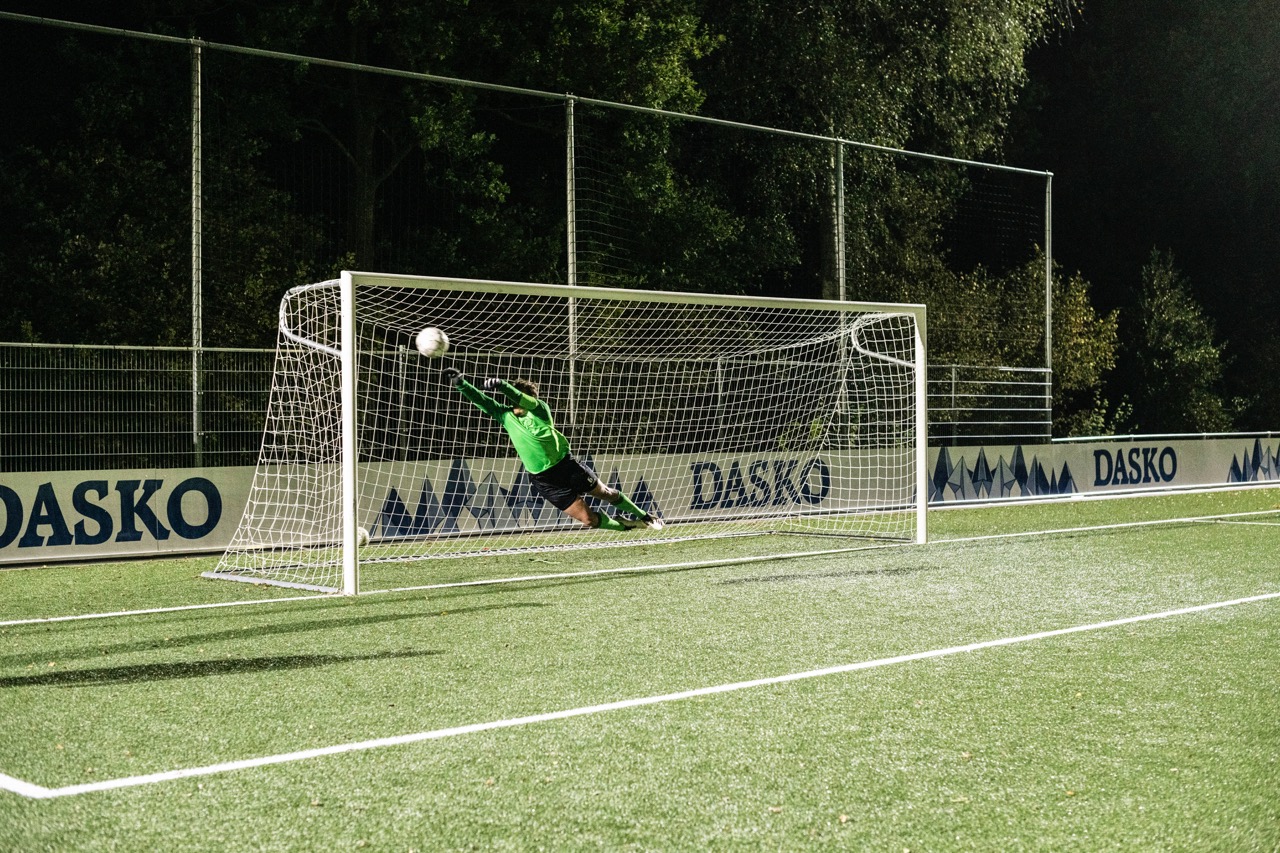 action shot of a goal keeper wearing a green jersey jumping to his right to catch the ball