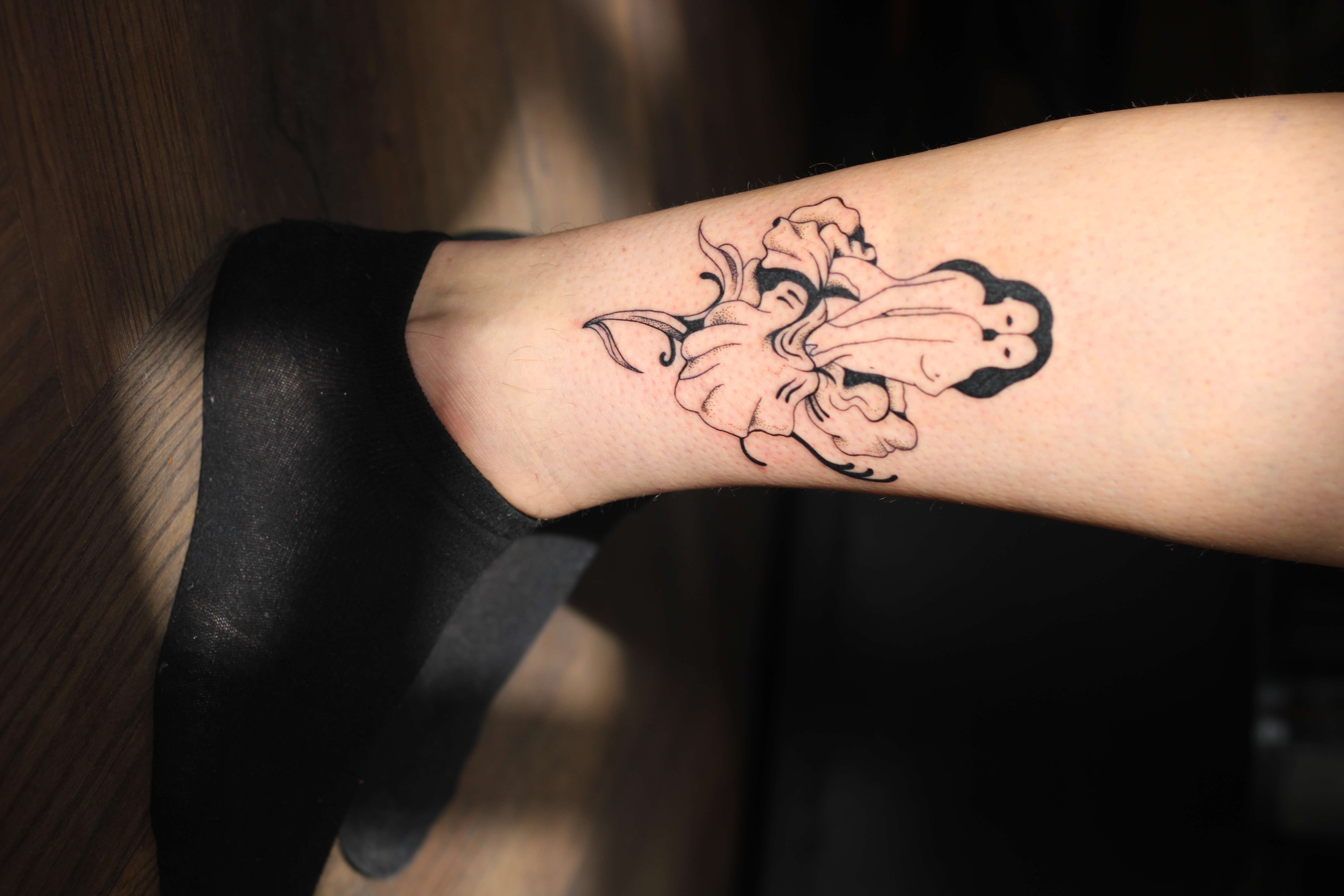Photo of two feet in black socks and a calve with a black tattoo of two women in a flower