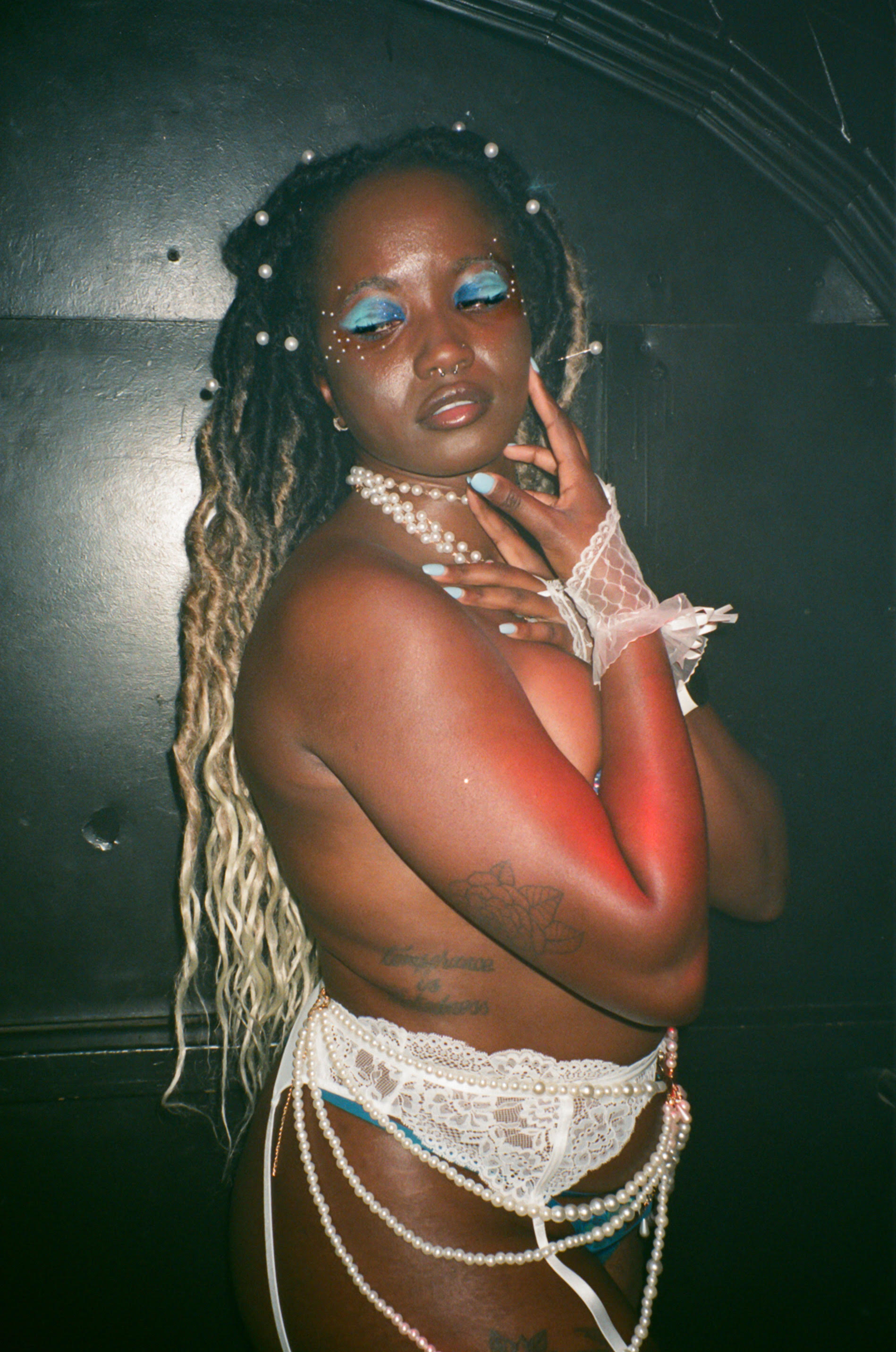 Person with dreads and blue eyeshadow in white lace lingerie