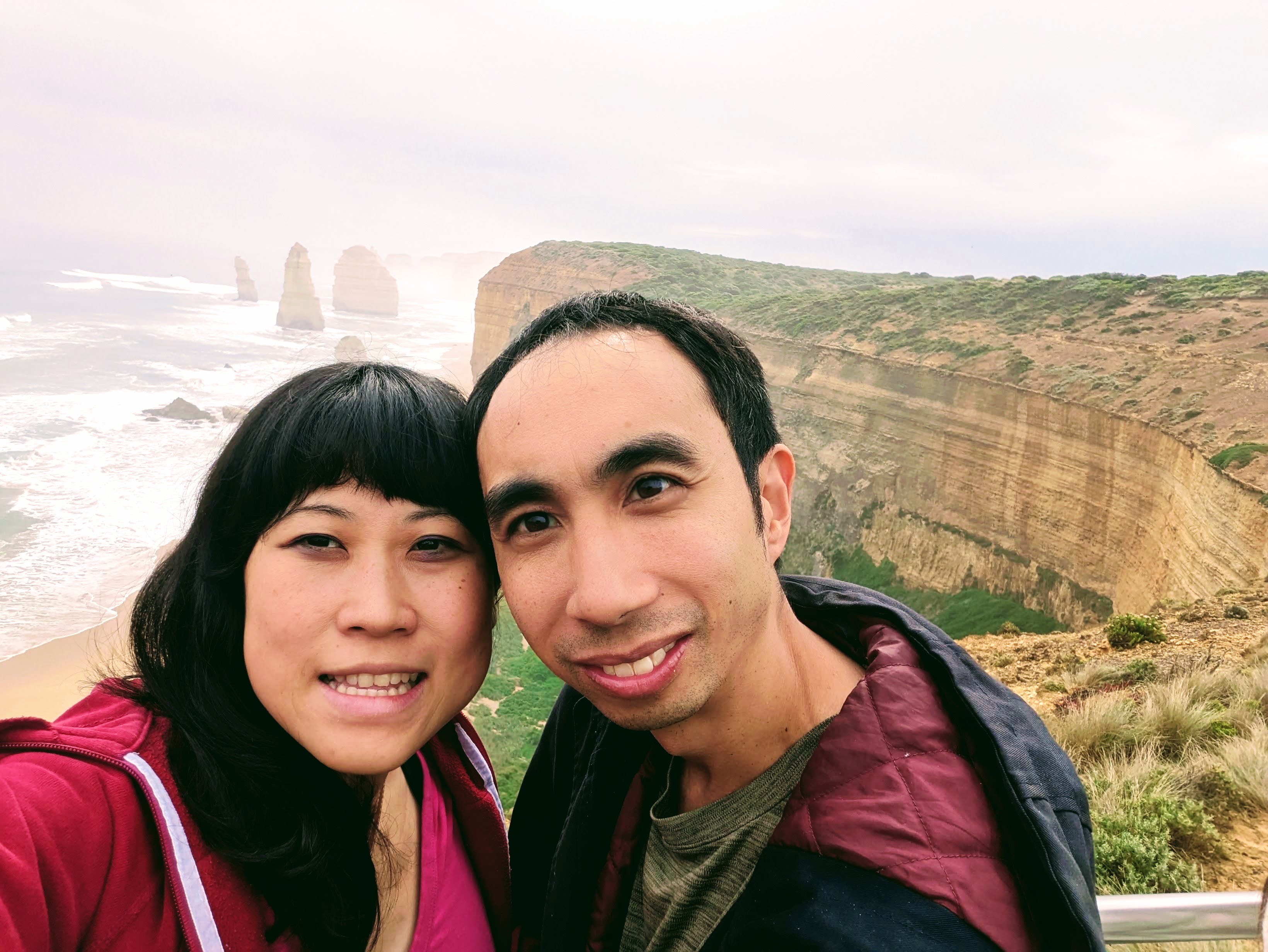 A woman and her husband pose for a photo on cliffs overlooking a misty sea.