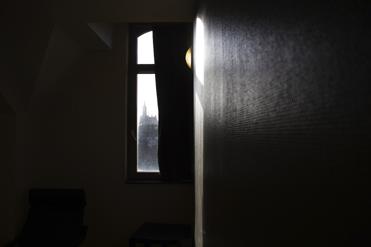 Transit, Brussels – A dark room with a vertical window showing a church somewhere in the distance