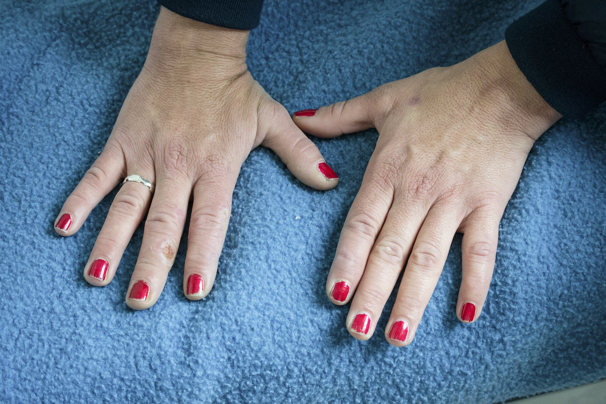 Transit, Brussels – close up of hands laying on a blue blanket. The nails are painted a metallic red and are slightly chipped.