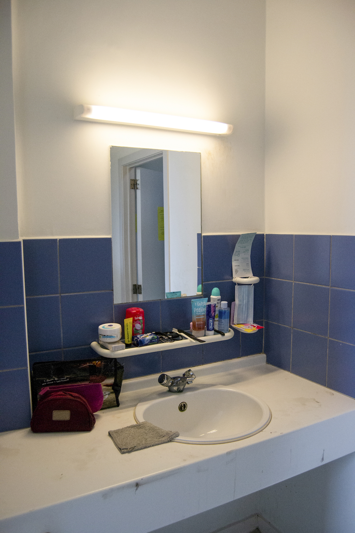 Transit, Brussels – close-up of a small sink in a room with blue tiles and a small mirror.