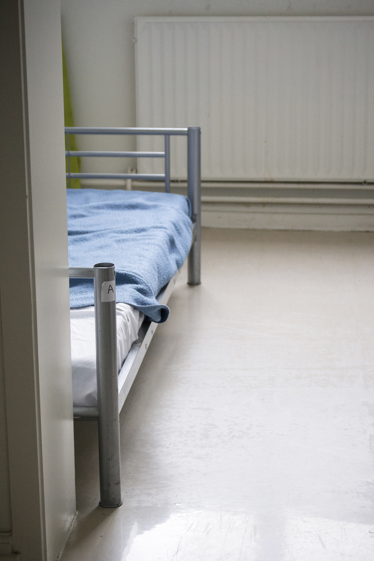 Transit, Brussels – Closeup of a bedroom with a single, metal-frame bad low to the ground.
