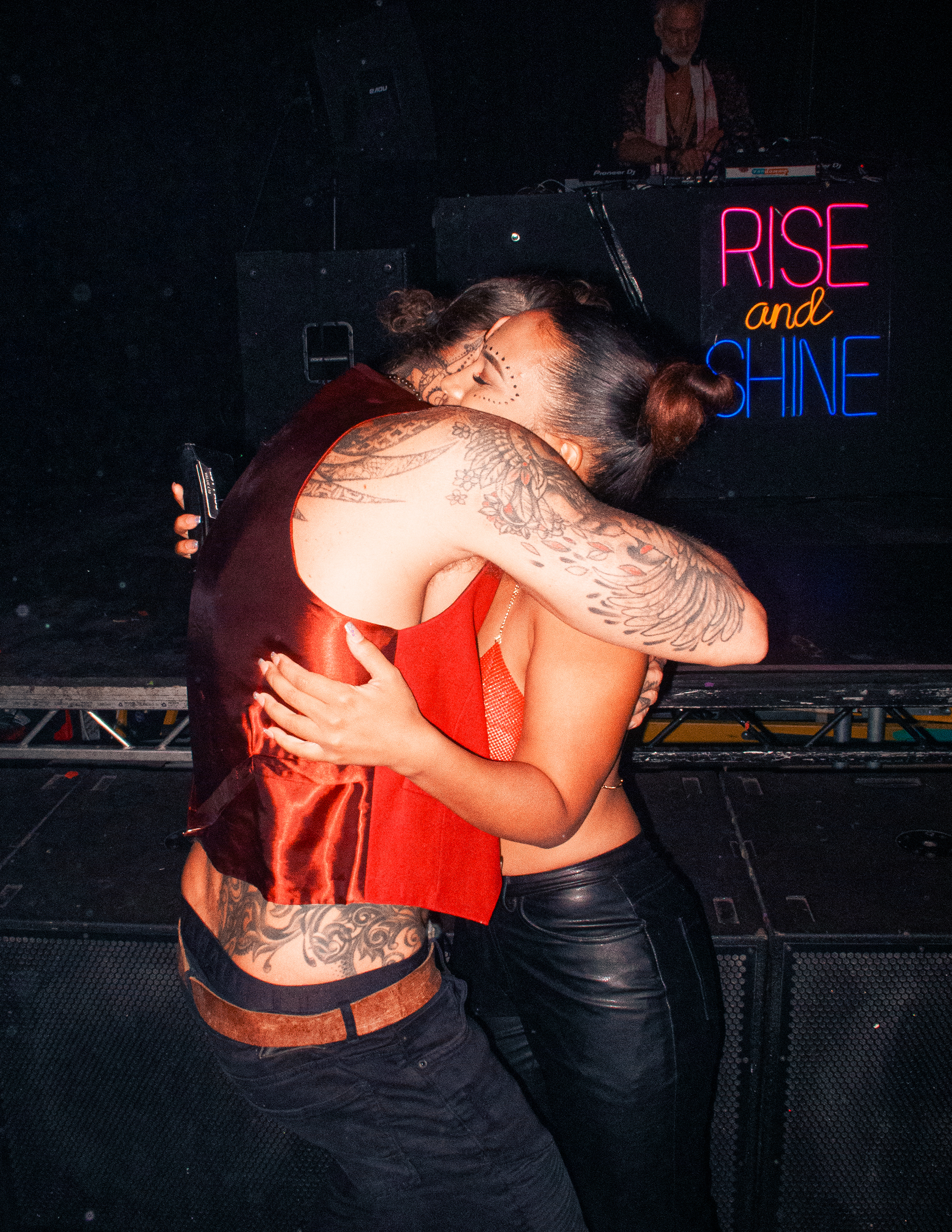 A tall topless man in an unbuttoned red waistcoat hugs a small, beautiful woman in leather jeans and a chainmail bralet.